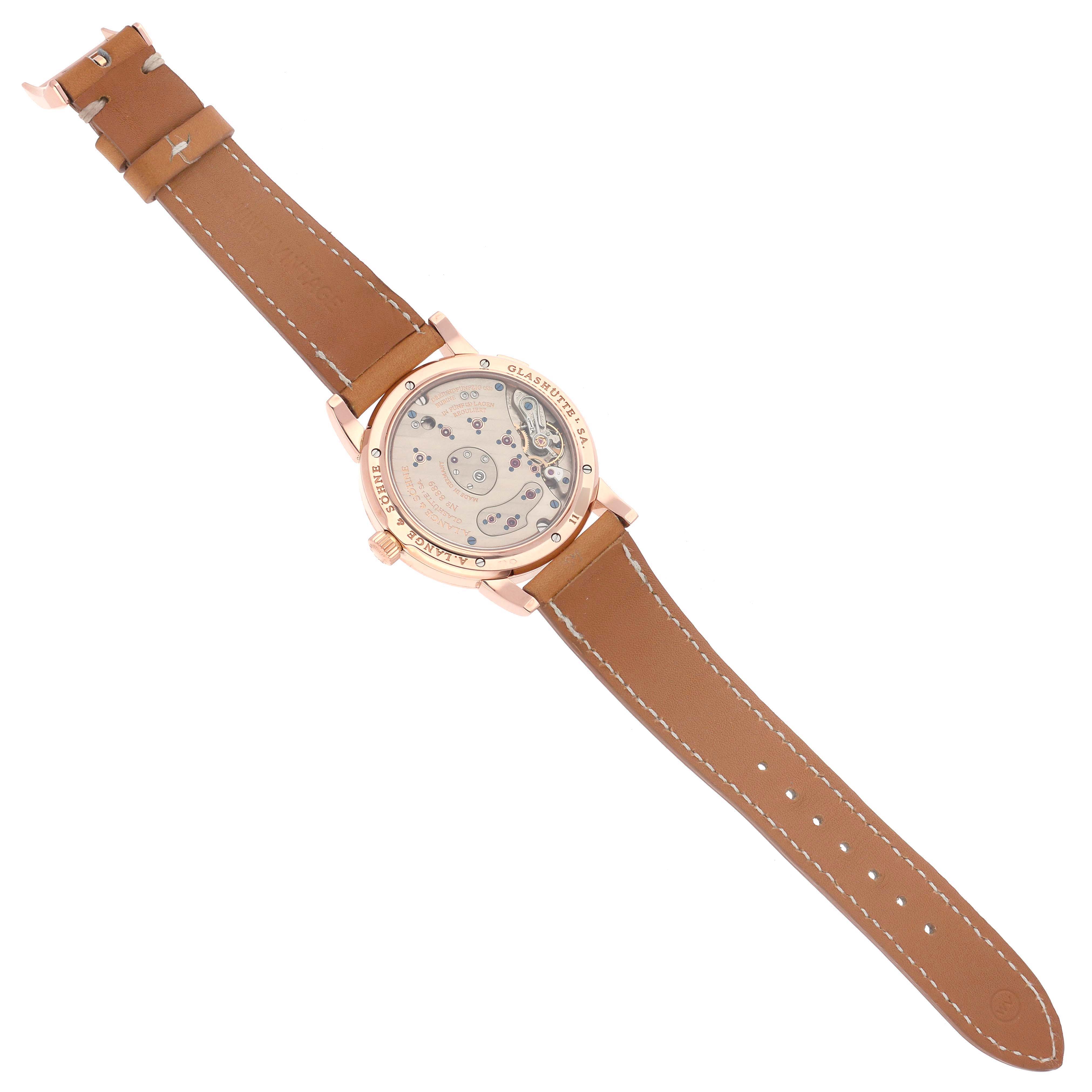 The image shows the back of the Lange 1 watch by A. Lange & Söhne, highlighting the movement and brown leather strap.