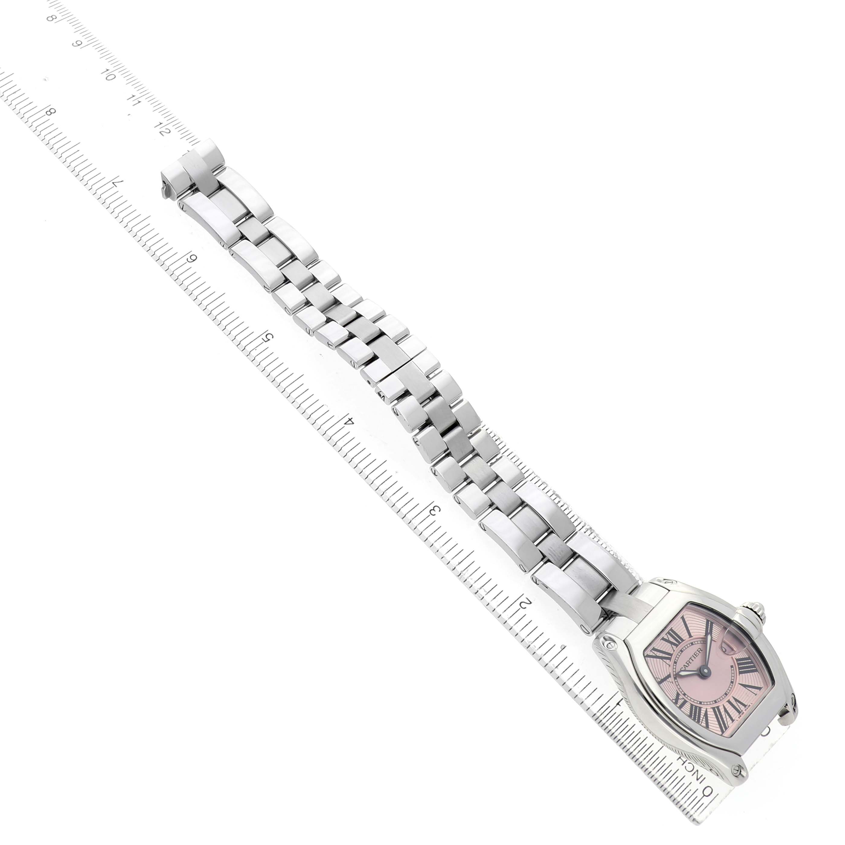 The Cartier Roadster W62017V3 Women's Stainless Steel Pink Dial watch is shown at an angle highlighting its face and full metal bracelet alongside a ruler.