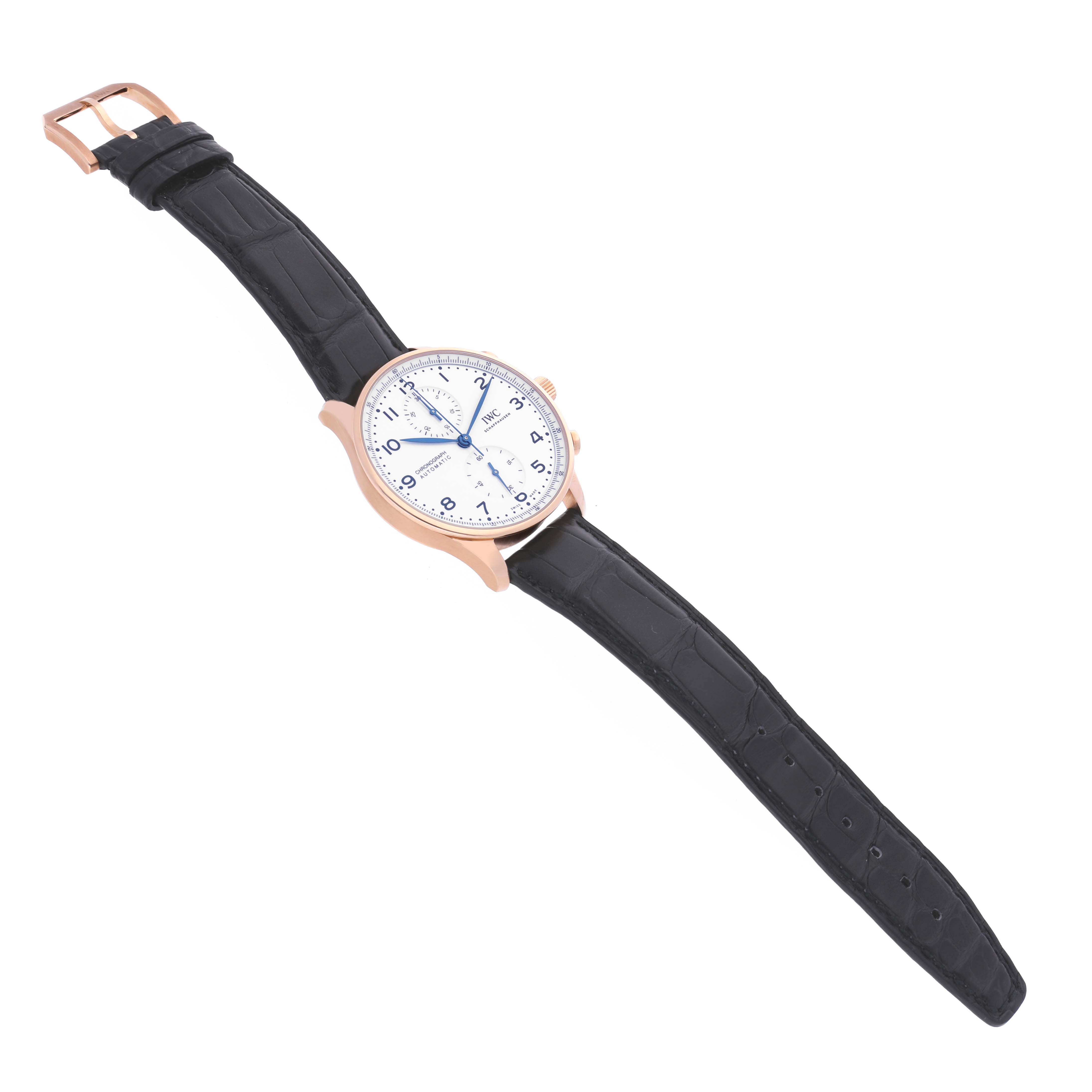 The IWC Portuguese IW371603 Men's Rose Gold White Dial IW371603 Men's Rose Gold White Dial watch is shown at a slight overhead angle, displaying the face, strap, and buckle.