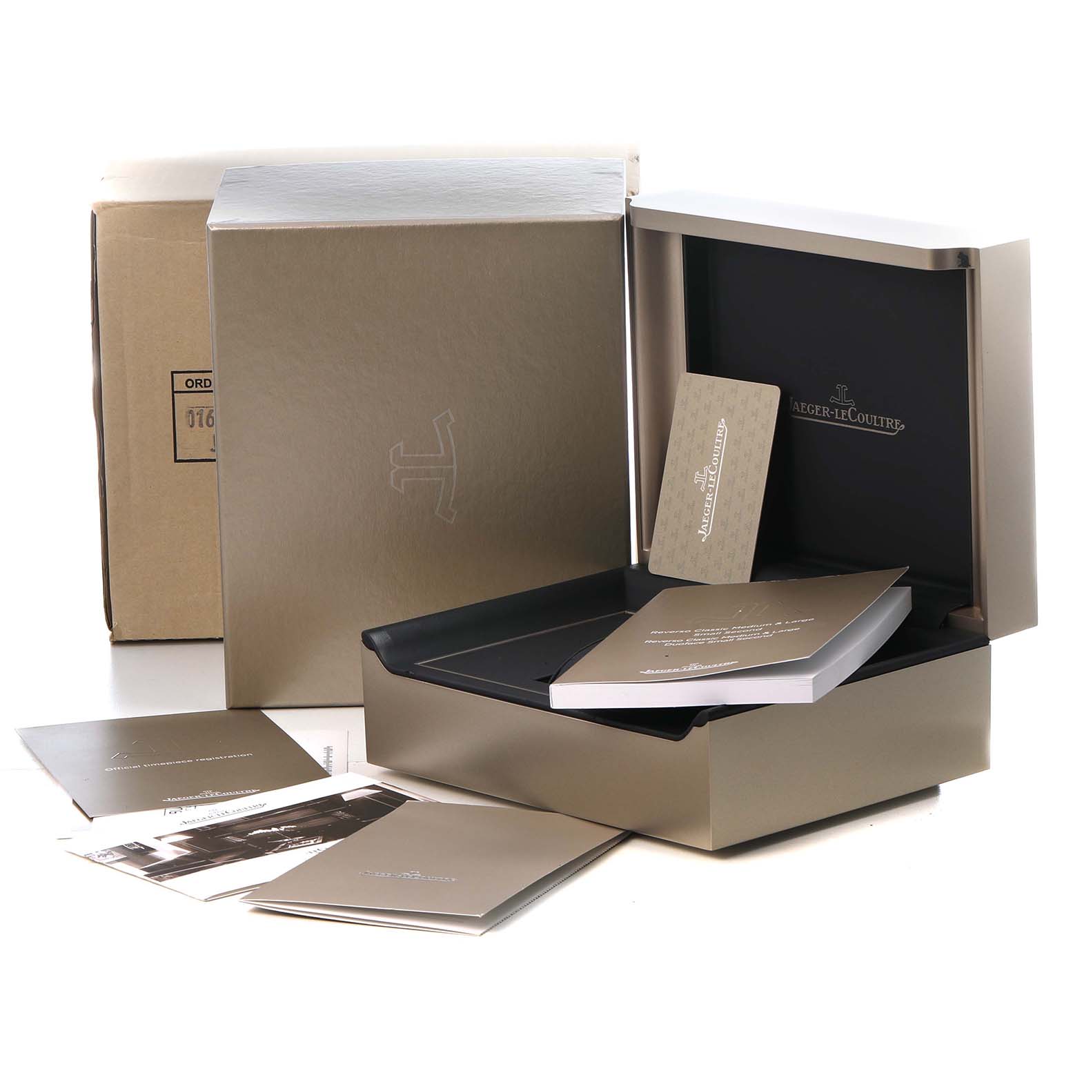 The image shows the packaging and manuals for a Jaeger-LeCoultre Reverso watch, including a box and documentation.