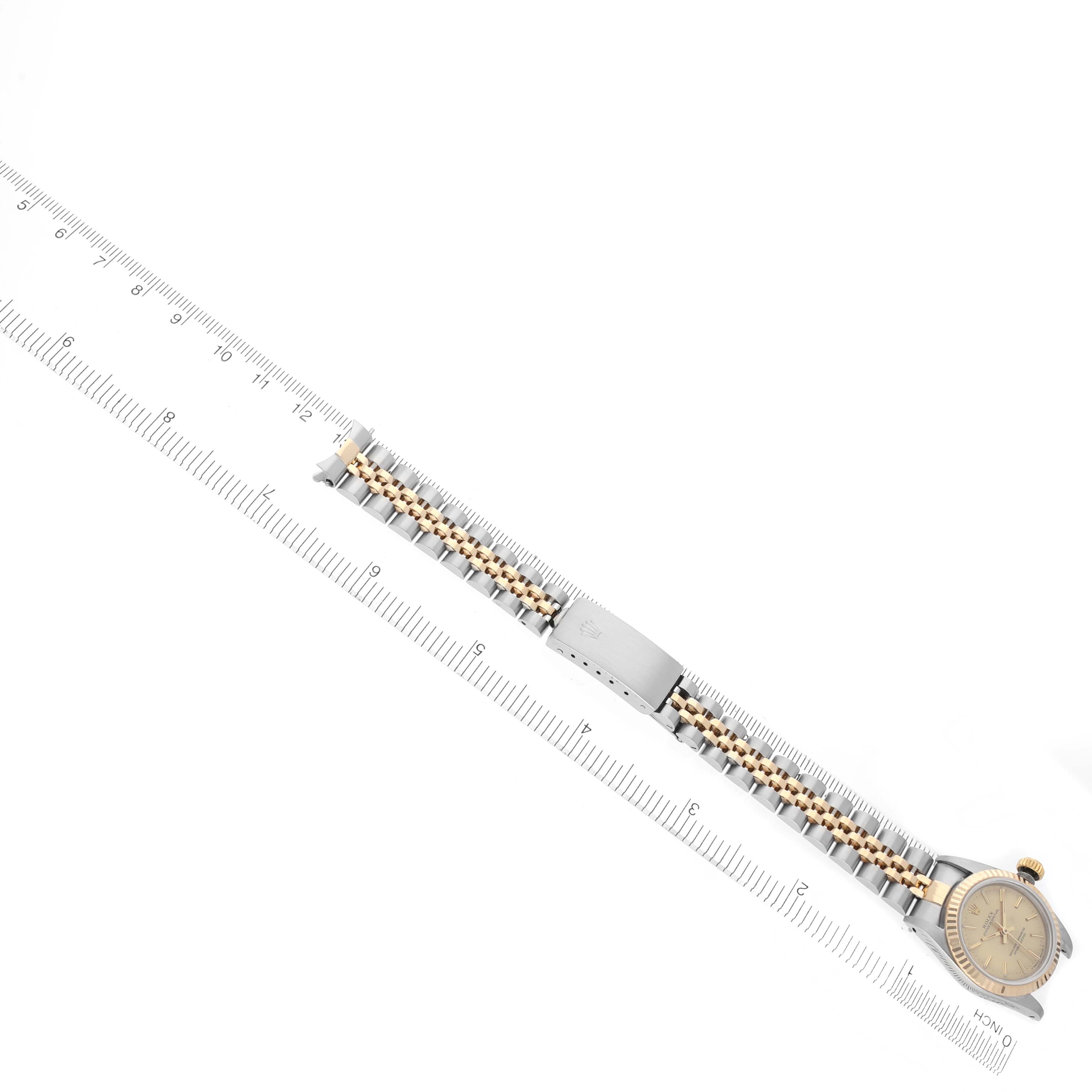 The Rolex Oyster Perpetual 67193 Women's Steel and Gold (two tone) Champagne Dial 67193 Women's Steel and Gold (two tone) Champagne Dial watch is shown from an angled top view, showcasing its bracelet and face alongside a ruler.