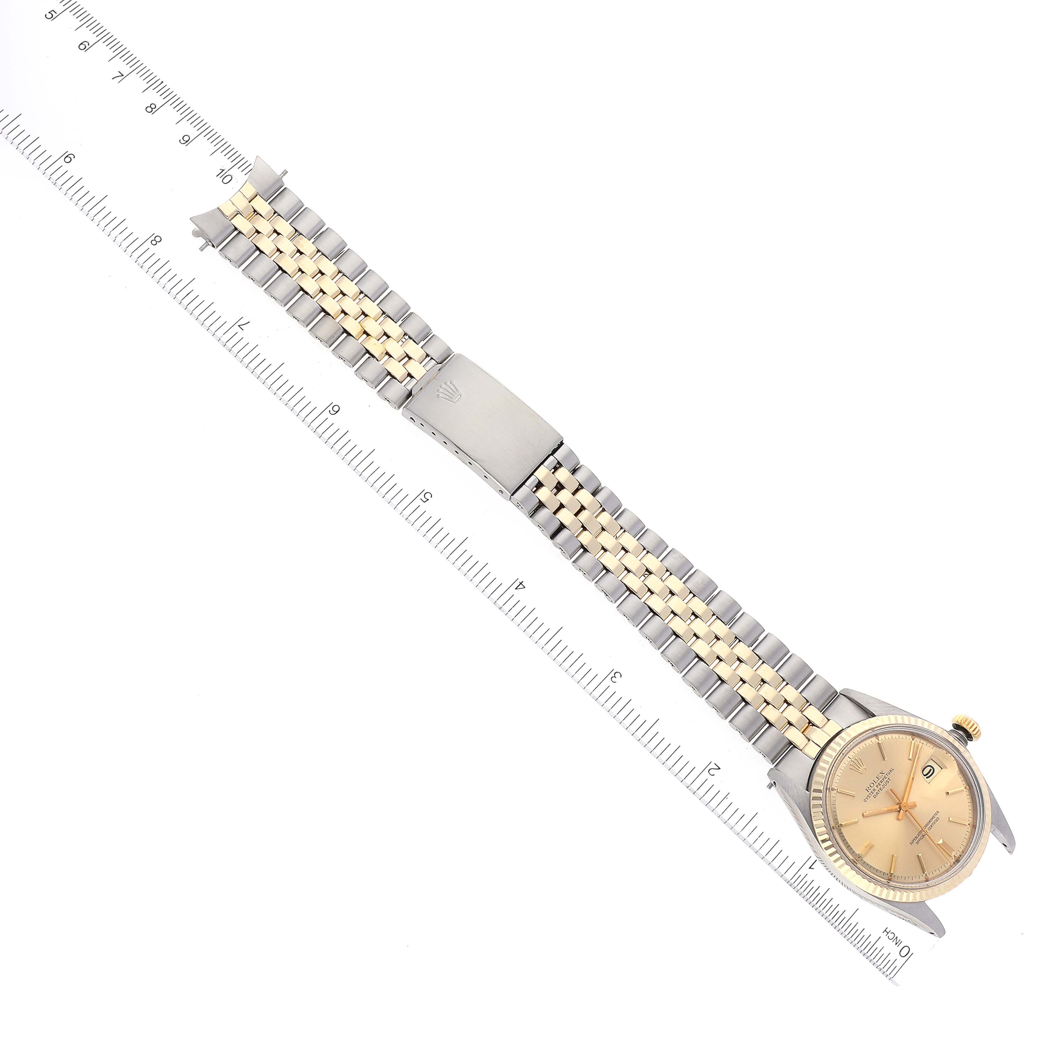 The Rolex Datejust 1601 Men's Steel and Gold (two tone) Champagne Dial 1601 Men's Steel and Gold (two tone) Champagne Dial watch is shown from a top-down angle, displaying its full band and face alongside a measuring ruler.
