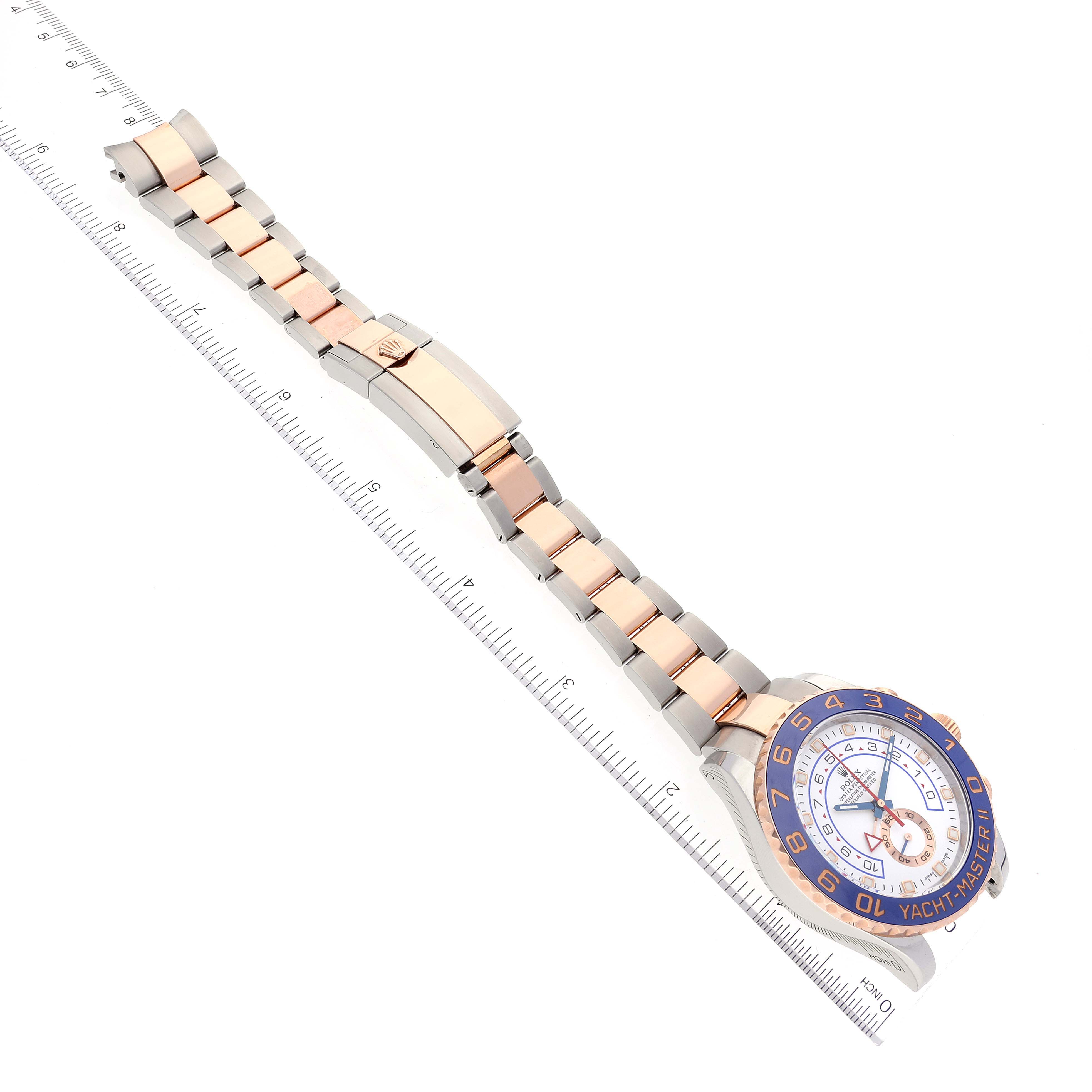 The image shows a Rolex Yacht-Master 116681 Men
s Steel and Gold (two tone) White Dial 116681 Men
s Steel and Gold (two tone) White Dial watch laid flat with its face, bracelet, and clasp visible alongside a measuring ruler.