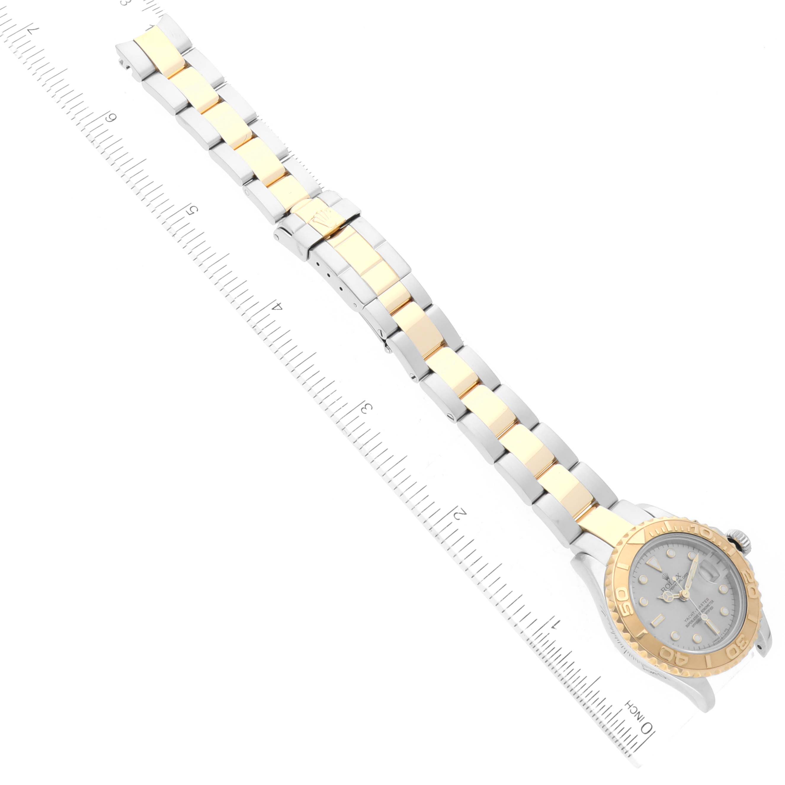 The Rolex Yacht-Master 69623 Women
s Steel and Gold (two tone) Grey Dial 69623 Women
s Steel and Gold (two tone) Grey Dial watch is shown from a top-down angle, displaying the face and full bracelet, with a ruler for scale.