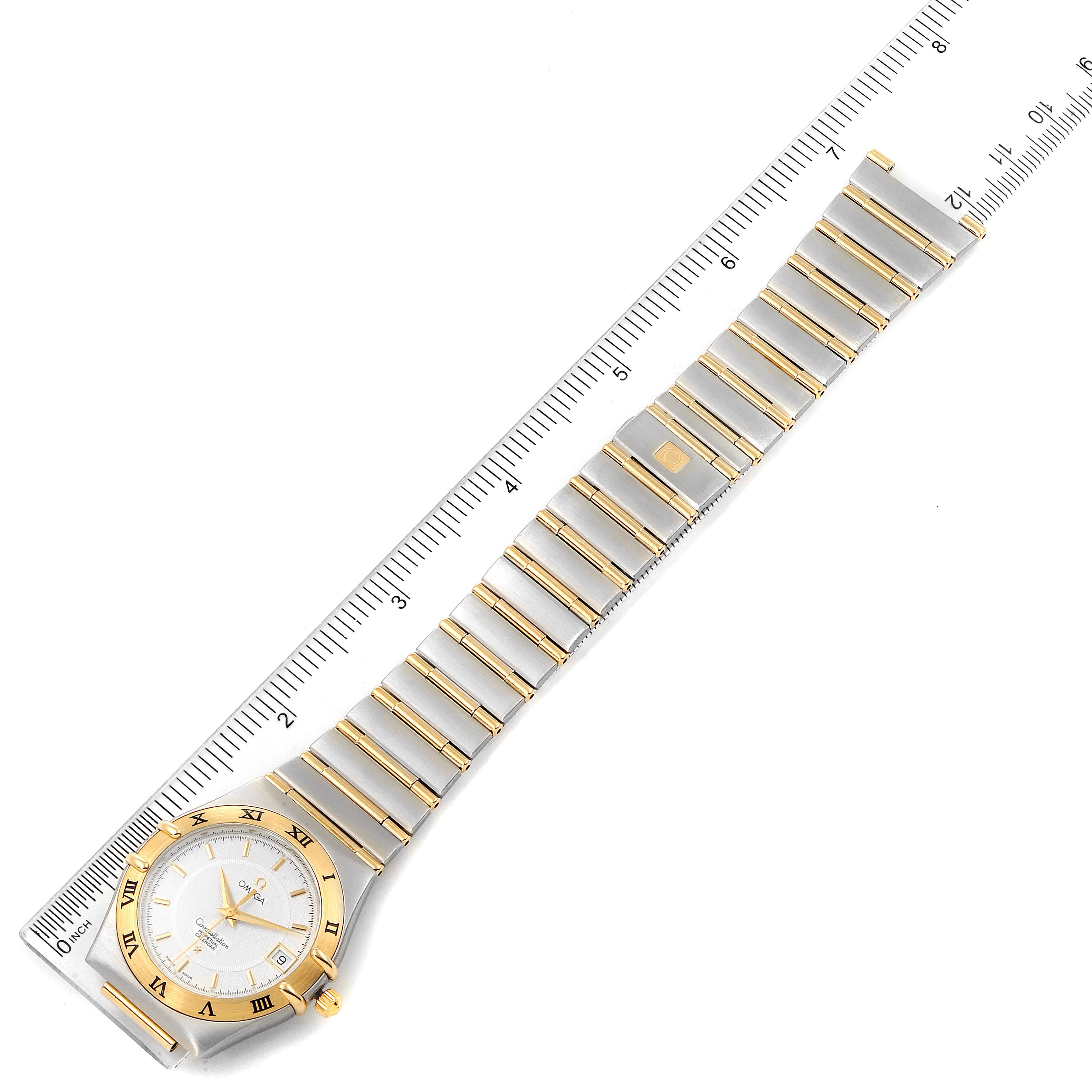 The image shows a top-down view of an Omega Constellation 1252.30.00 Men's Steel and Gold (two tone) Silver Dial 1252.30.00 Men's Steel and Gold (two tone) Silver Dial watch, highlighting the dial, bezel, and bracelet next to a ruler.