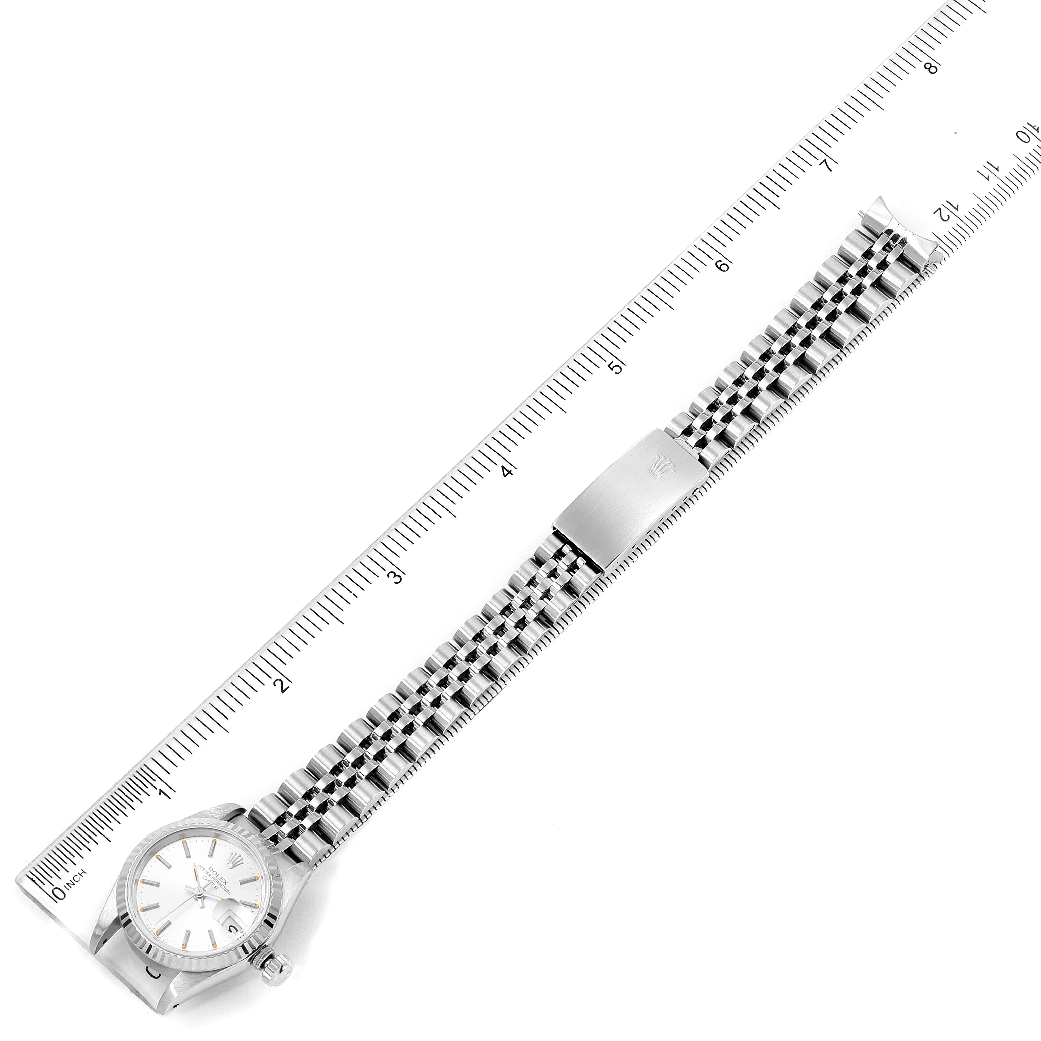 The Rolex Date 69174 Women's Stainless Steel Silver Dial 69174 Women's Stainless Steel Silver Dial model watch is shown laying flat, displaying its face, bracelet, and clasp, alongside a ruler for scale.