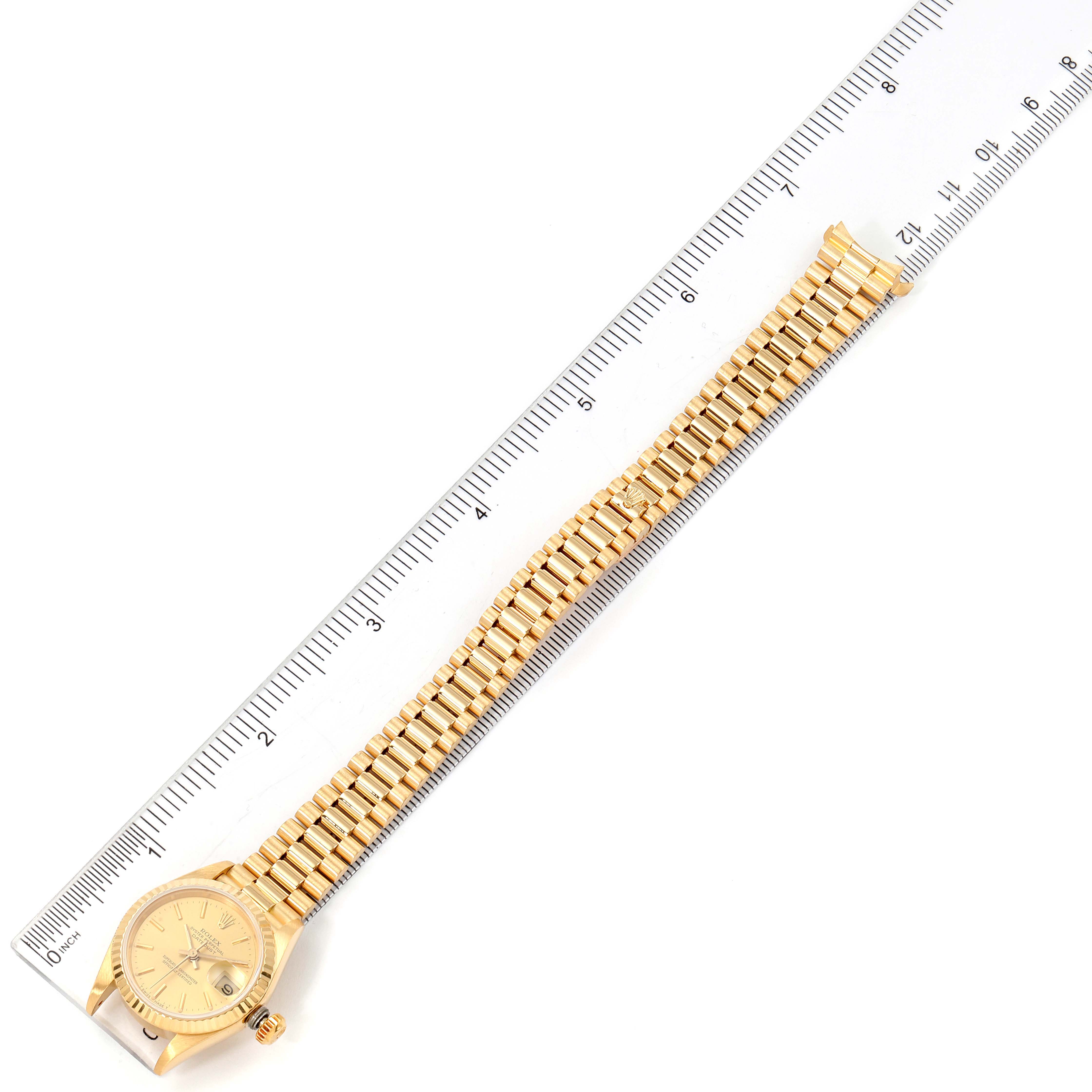 The image shows a Rolex President 69178 Women
s Yellow Gold Champagne Dial 69178 Women
s Yellow Gold Champagne Dial watch from a top-down angle, highlighting its gold bracelet and watch face next to a ruler for scale.