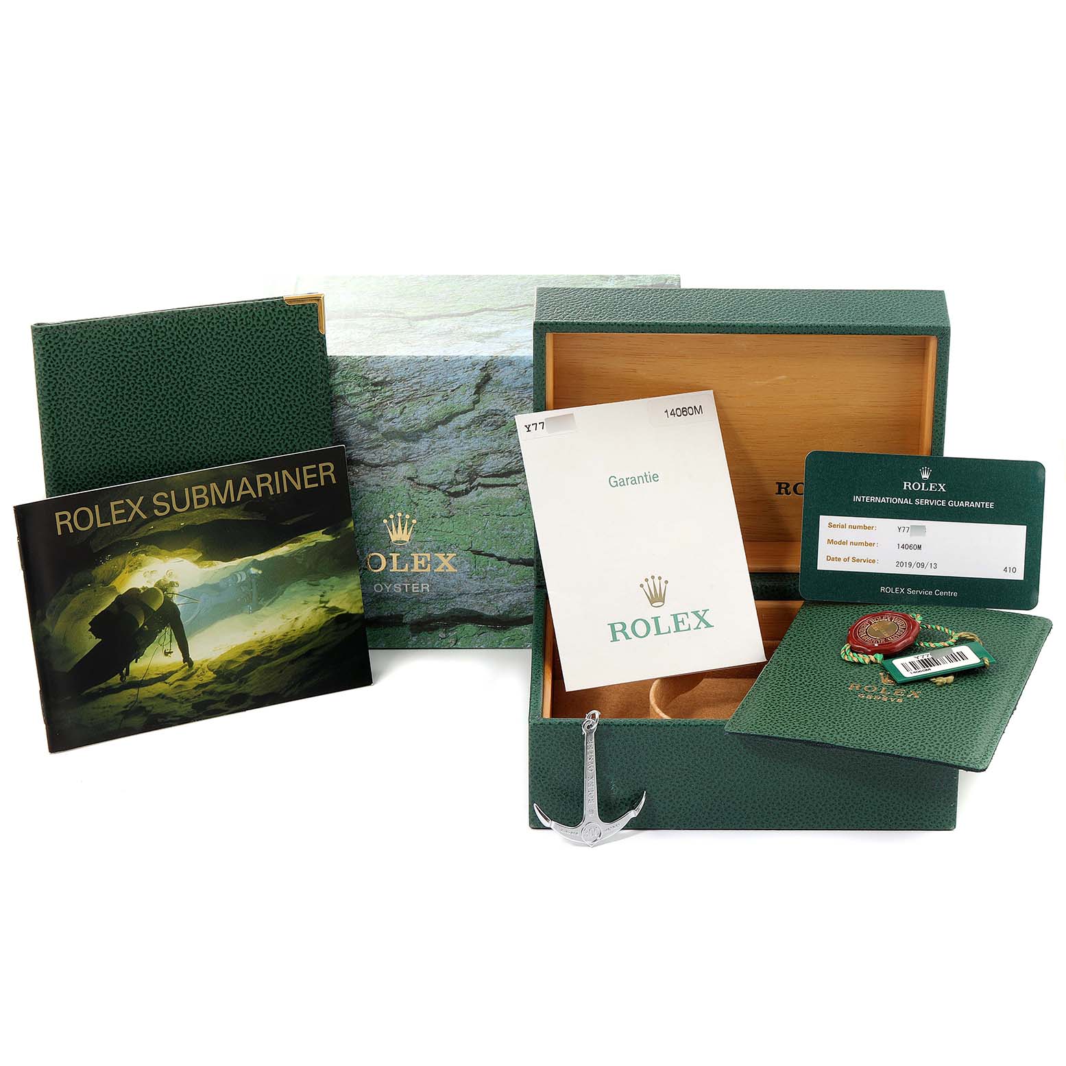 The image shows the packaging and accessories for a Rolex Submariner 14060 Men
s Stainless Steel Black Dial 14060 Men
s Stainless Steel Black Dial, including the box, booklet, warranty card, anchor charm, and tags.