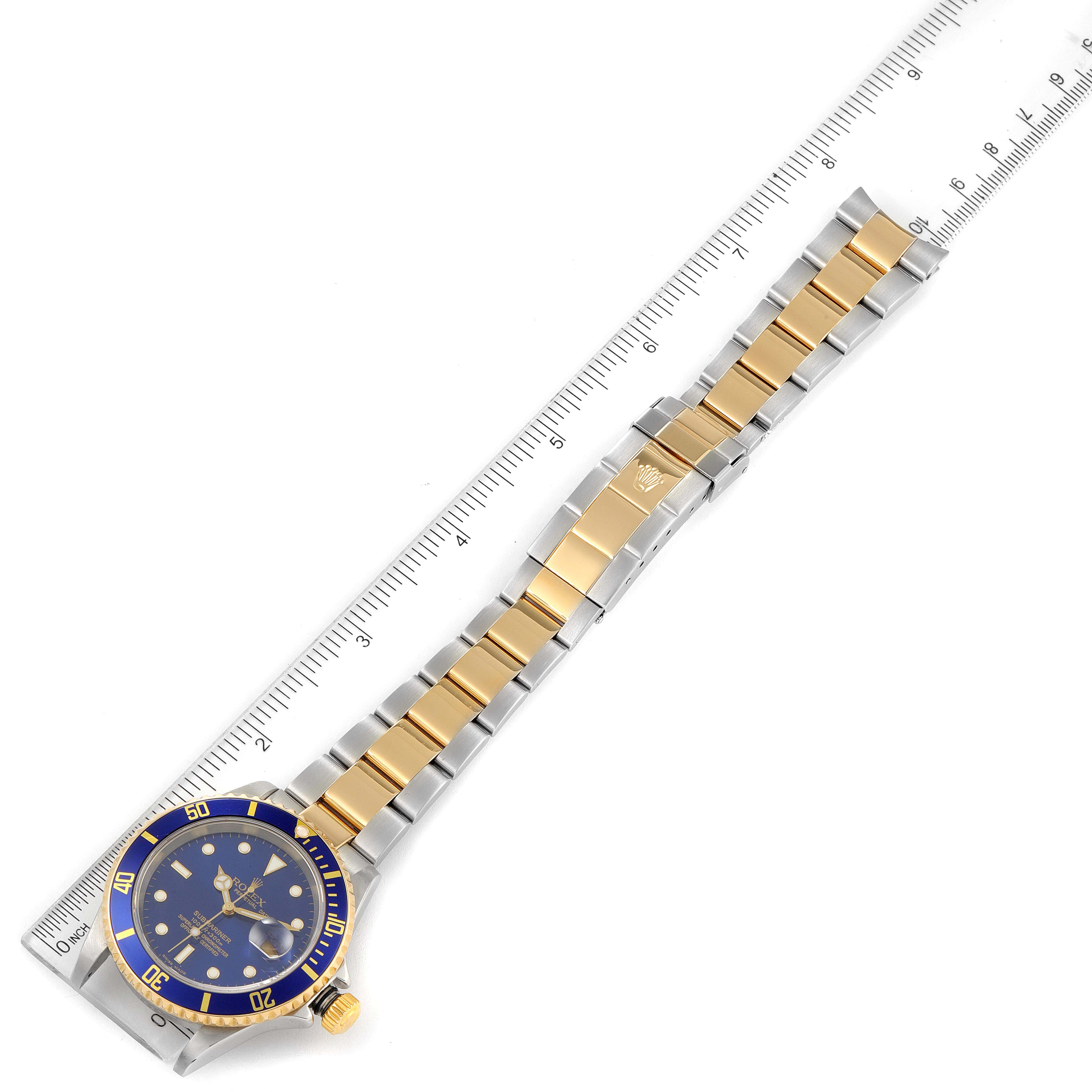 The image displays a full view of the Rolex Submariner 16613 Men's Steel and Gold (two tone) Blue Dial 16613 Men's Steel and Gold (two tone) Blue Dial watch, including its gold and steel bracelet, placed alongside a ruler.