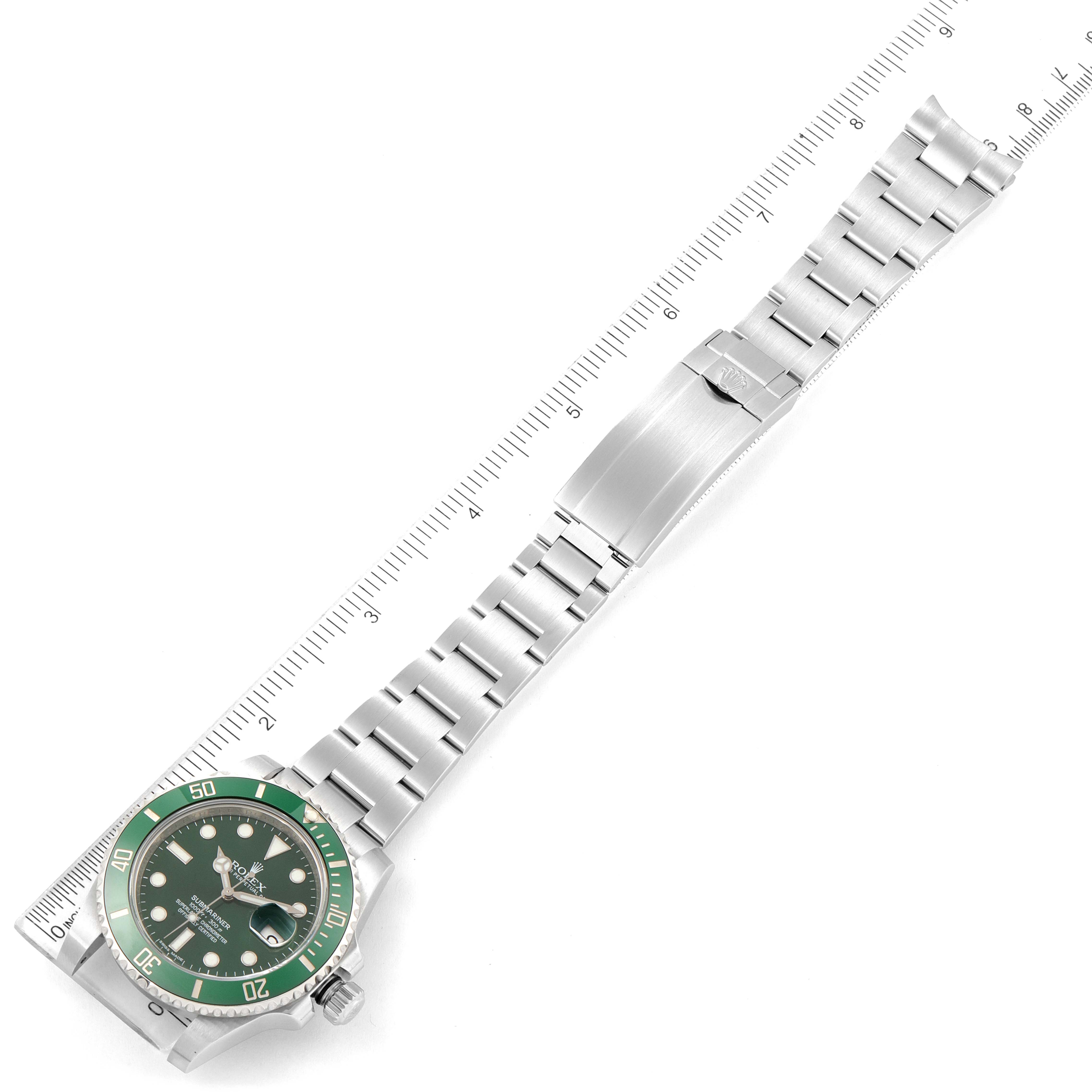 This image shows a Rolex Submariner 116610LV Men
s Stainless Steel Green Dial 116610LV Men
s Stainless Steel Green Dial watch laid flat with a ruler next to it, displaying its face, bezel, and bracelet prominently.