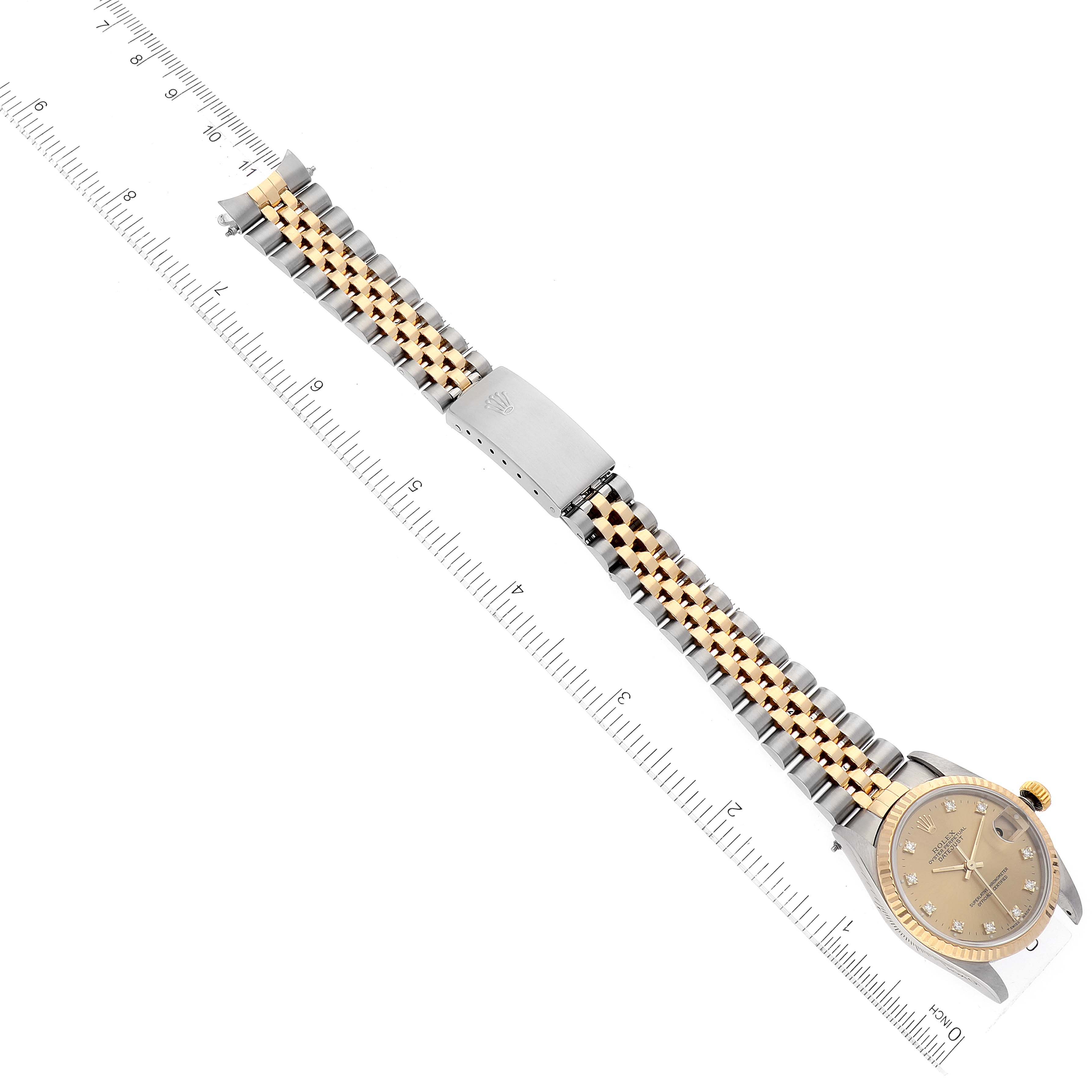 The image shows a full view of a Rolex Mid-Size 68273 Women
s Steel and Gold (two tone) Champagne Dial 68273 Women
s Steel and Gold (two tone) Champagne Dial watch laid flat with a ruler for scale, featuring its face, band, and clasp.