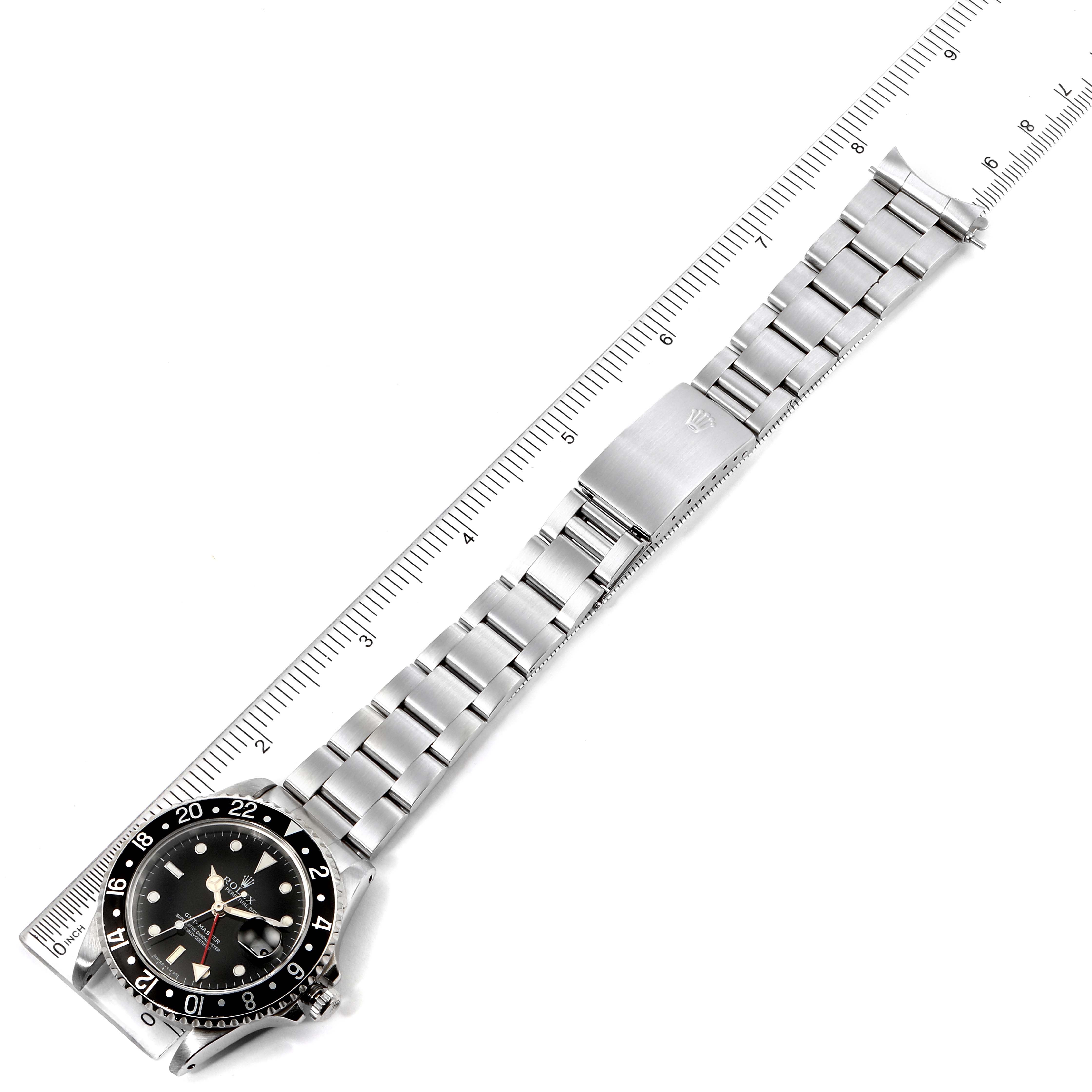 This image shows a Rolex GMT-Master 16700 Men's Stainless Steel Black Dial 16700 Men's Stainless Steel Black Dial watch laid flat with a metal bracelet, displayed alongside a ruler.