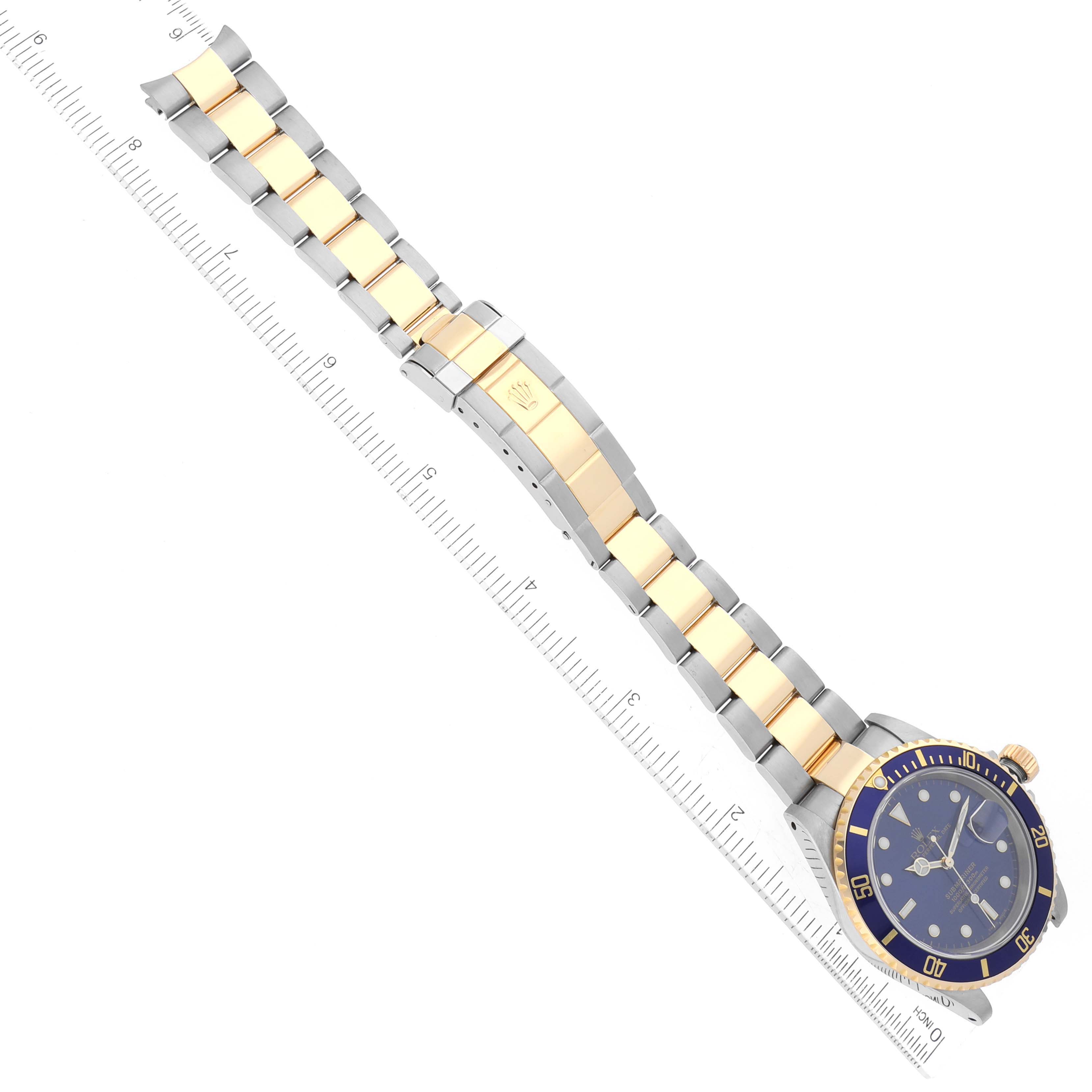 The image shows a Rolex Submariner 16613LB Men
s Steel and Gold (two tone) Blue Dial 16613LB Men
s Steel and Gold (two tone) Blue Dial watch laid out horizontally, highlighting the face, bezel, crown, and bracelet with a ruler for scale.