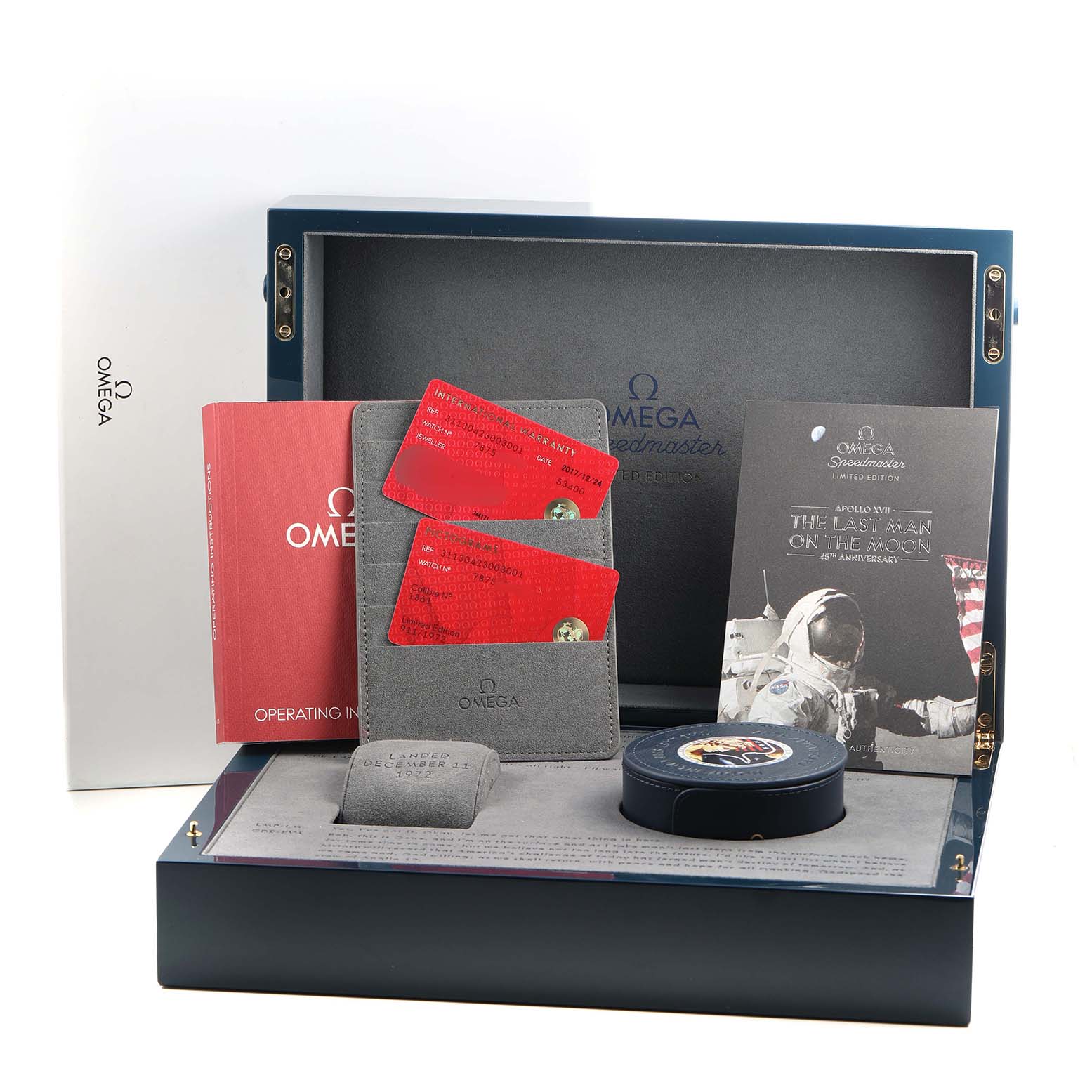 The Omega Speedmaster 311.30.42.30.03.001 Men's Stainless Steel Blue Dial packaging is shown frontally, including manuals, cards, a case, and themed documentation.