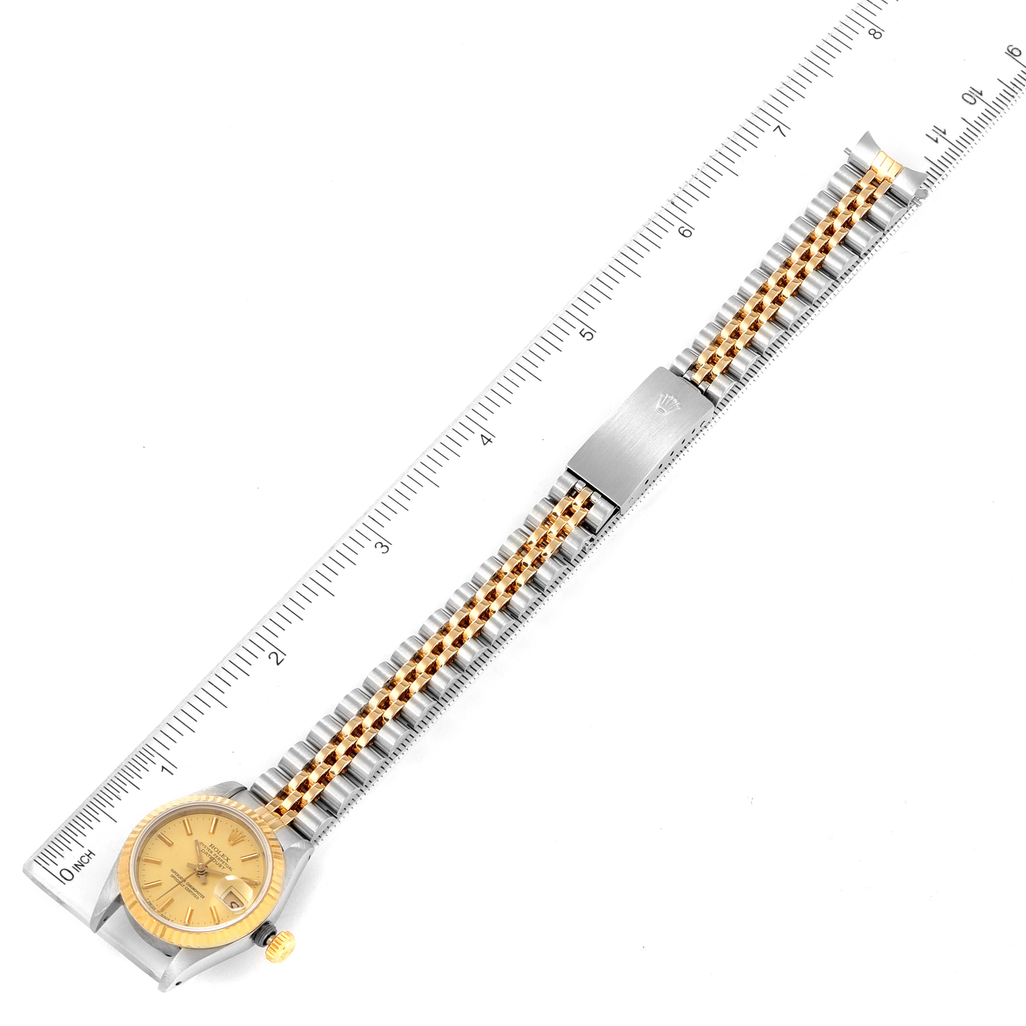 The image shows a top-down view of a Rolex Datejust 69173 Women
s Steel and Gold (two tone) Champagne Dial 69173 Women
s Steel and Gold (two tone) Champagne Dial watch with a ruler for scale, highlighting its face, bracelet, and clasp.