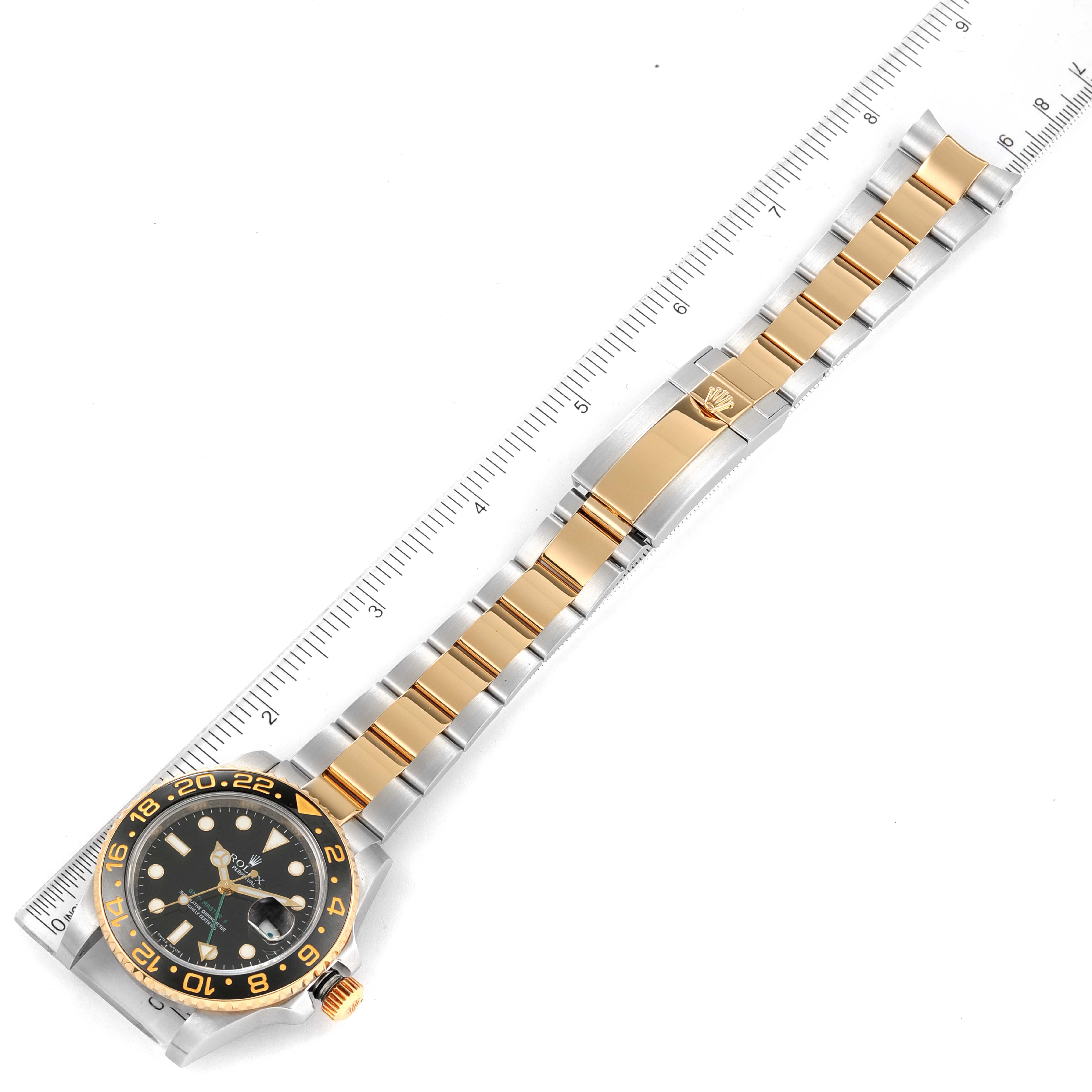 The image shows a Rolex GMT-Master 116713 Men's Steel and Gold (two tone) Black Dial 116713 Men's Steel and Gold (two tone) Black Dial watch lying flat, highlighting its bezel, dial, and two-tone bracelet alongside a ruler for scale.