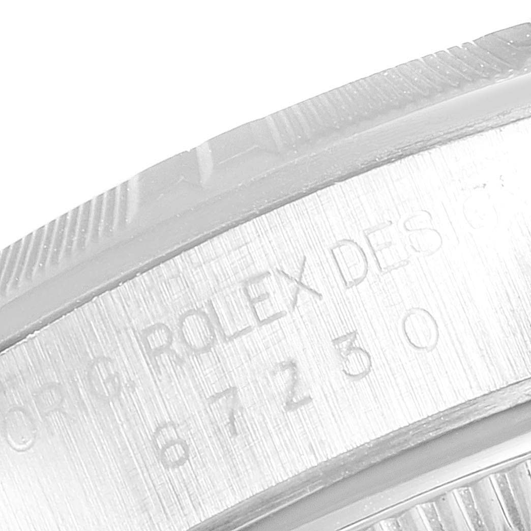 The image shows a close-up of the side of a Rolex Oyster Perpetual 67230 Women's Stainless Steel Pink Dial 67230 Women's Stainless Steel Pink Dial watch, focusing on the engraved design and serial number.