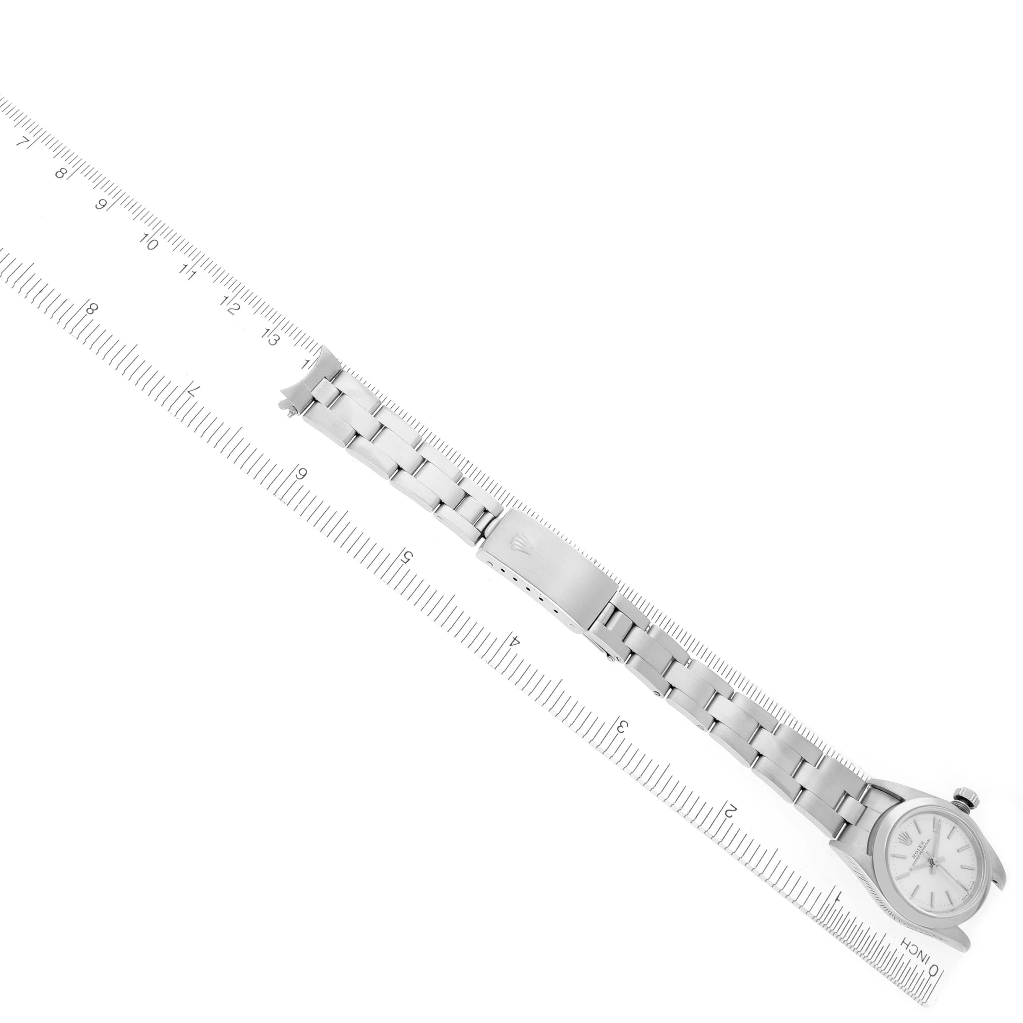 The Rolex Oyster Perpetual 76080 Women's Stainless Steel Silver Dial 76080 Women's Stainless Steel Silver Dial watch is shown diagonally with its stainless steel bracelet and clasp visible next to a ruler.