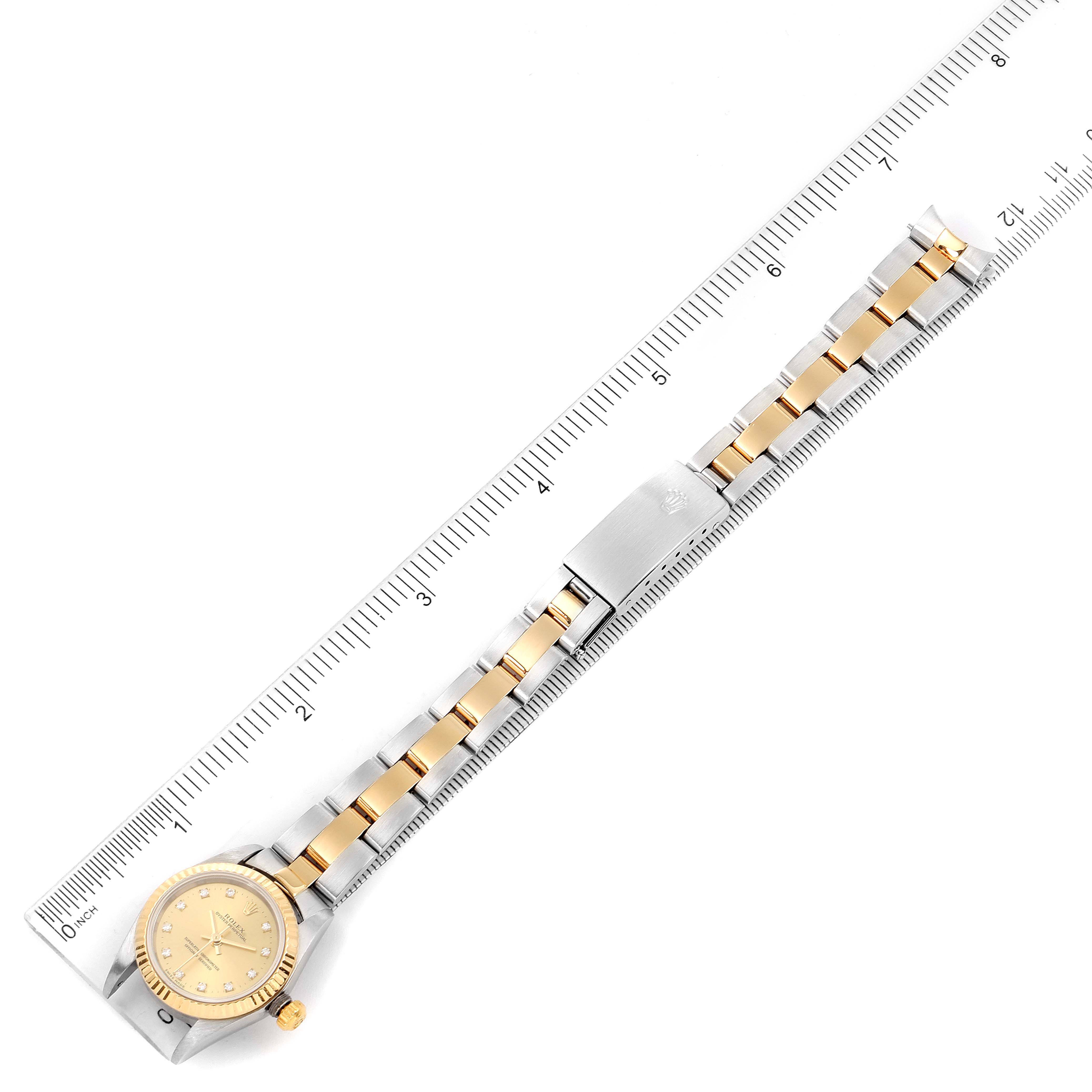 The image shows a top-down view of a Rolex Oyster Perpetual 76193 Women
s Steel and Gold (two tone) Champagne Dial 76193 Women
s Steel and Gold (two tone) Champagne Dial watch, displaying the face, bracelet, and clasp next to a ruler.