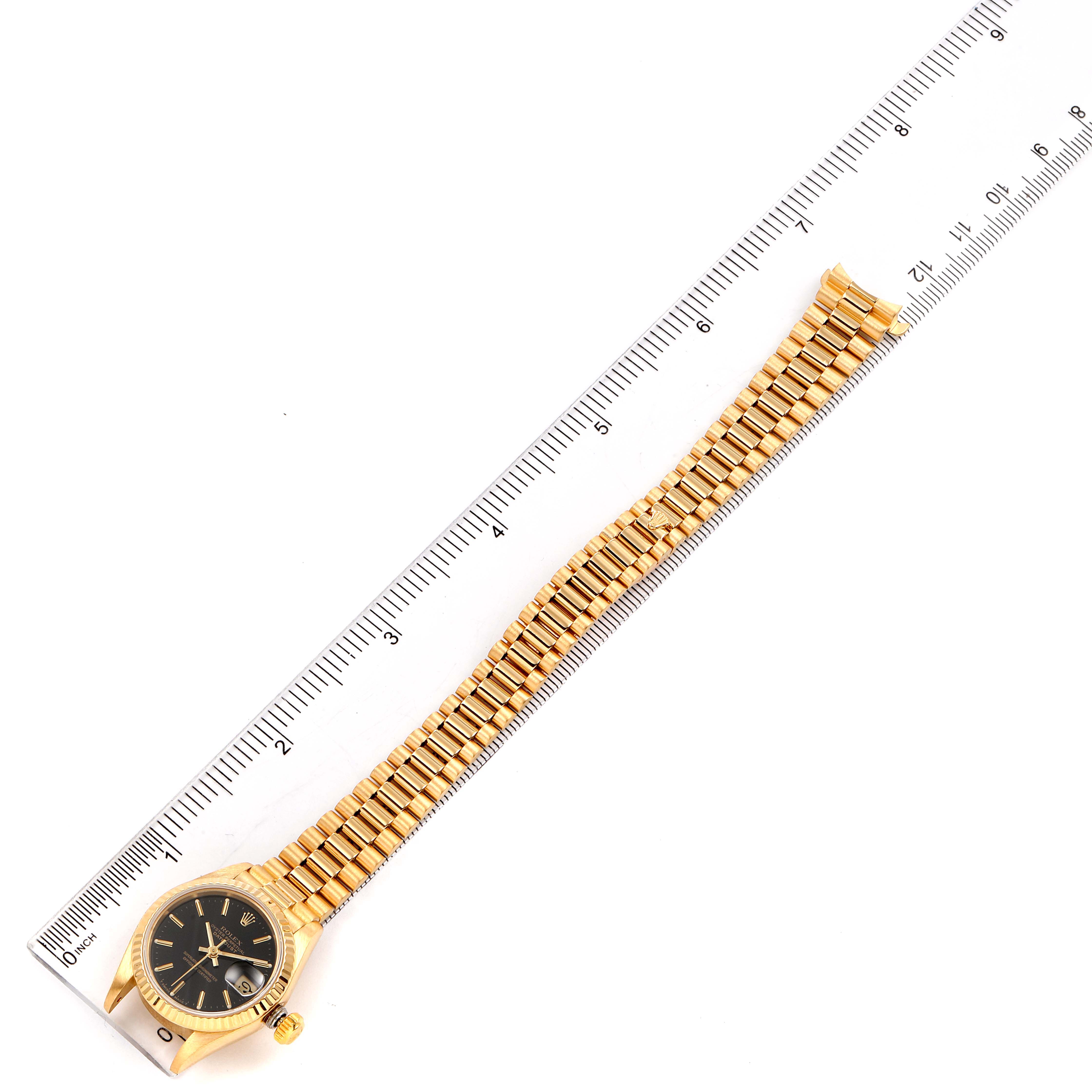 The image shows the full length of the Rolex President 69178 Women
s Yellow Gold Black Dial 69178 Women
s Yellow Gold Black Dial model watch, including the face, case, and bracelet, alongside a ruler.