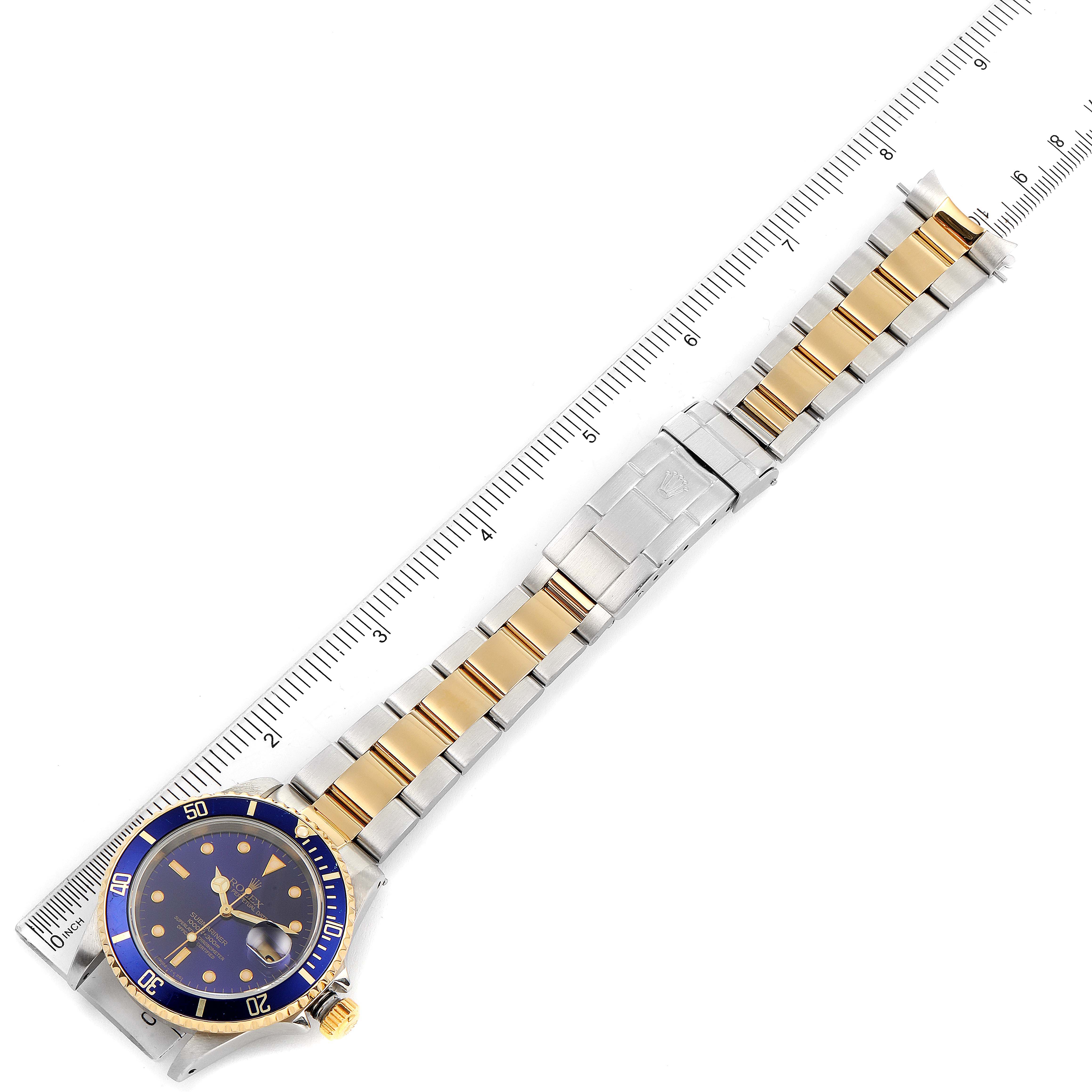 This image shows a Rolex Submariner 16613 Men
s Steel and Gold (two tone) Blue Dial 16613 Men
s Steel and Gold (two tone) Blue Dial watch from a top-down angle, displaying the dial, bezel, bracelet, and clasp against a ruler.