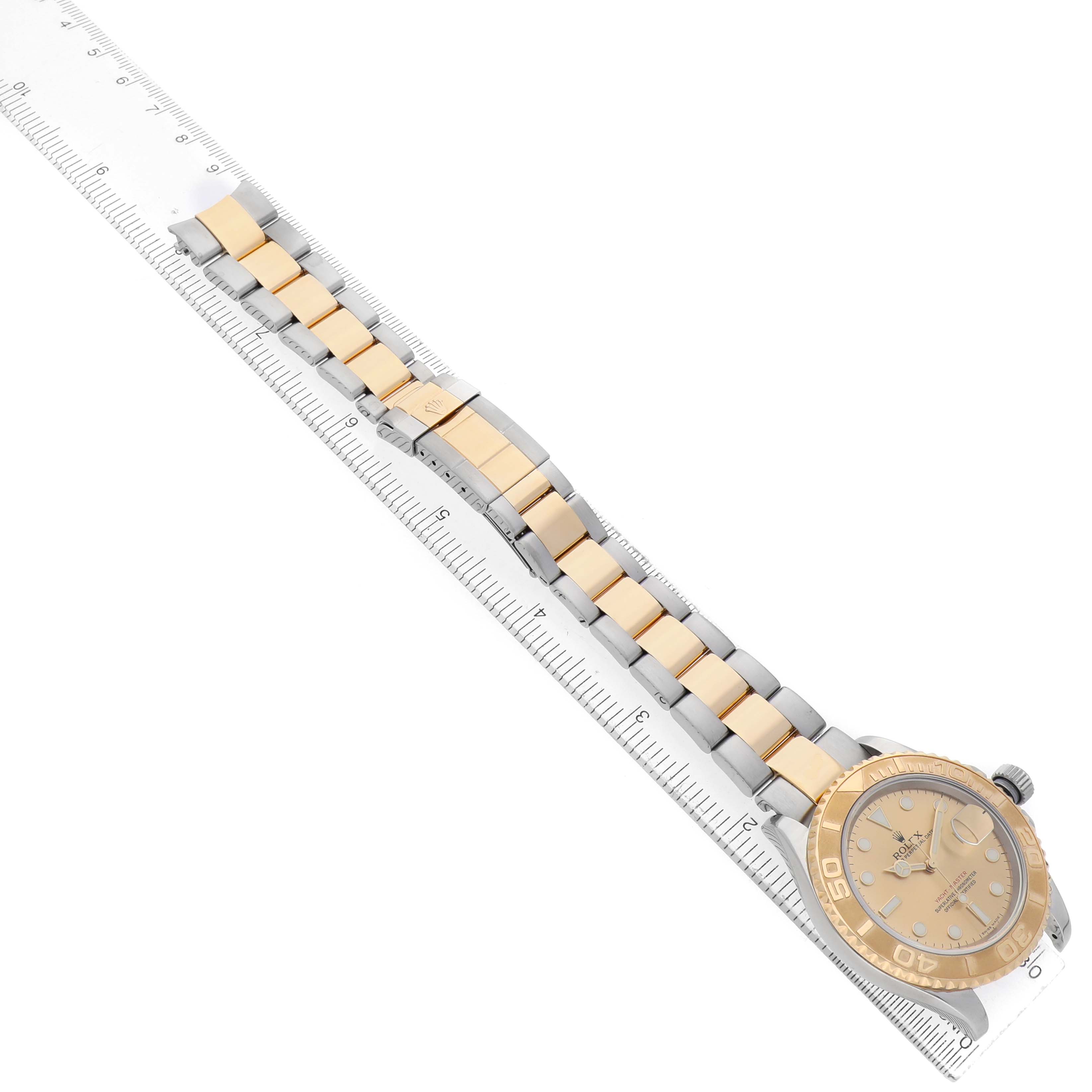 The Rolex Yacht-Master 77099 Men's Steel and Gold (two tone) Champagne Dial watch is shown at an angle displaying the full band, clasp, and dial, with a ruler for scale.