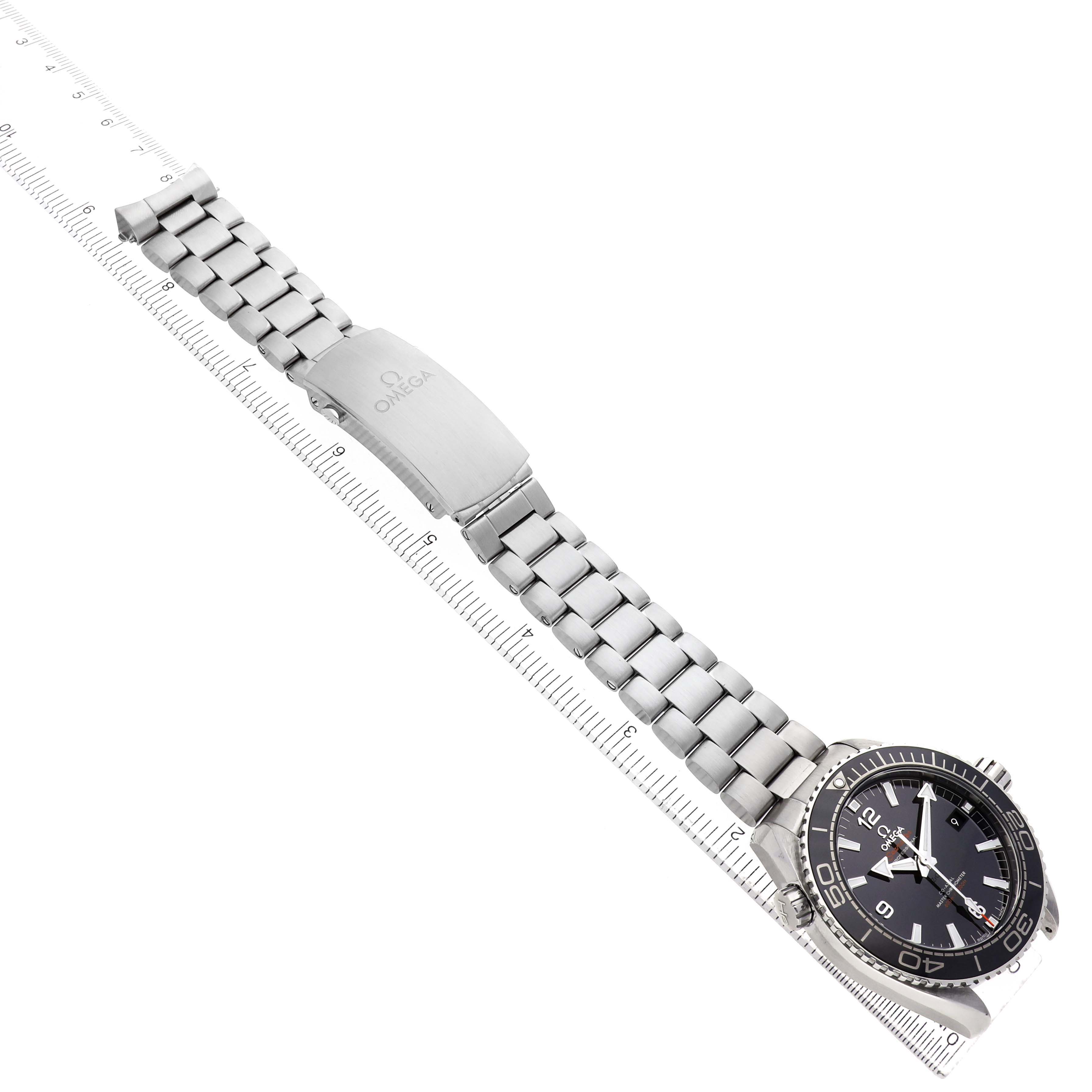 The Omega Planet Ocean 215.30.44.21.01.001 Men's Stainless Steel Black Dial watch is shown at an angle displaying the face, bezel, bracelet, and clasp on a ruler.