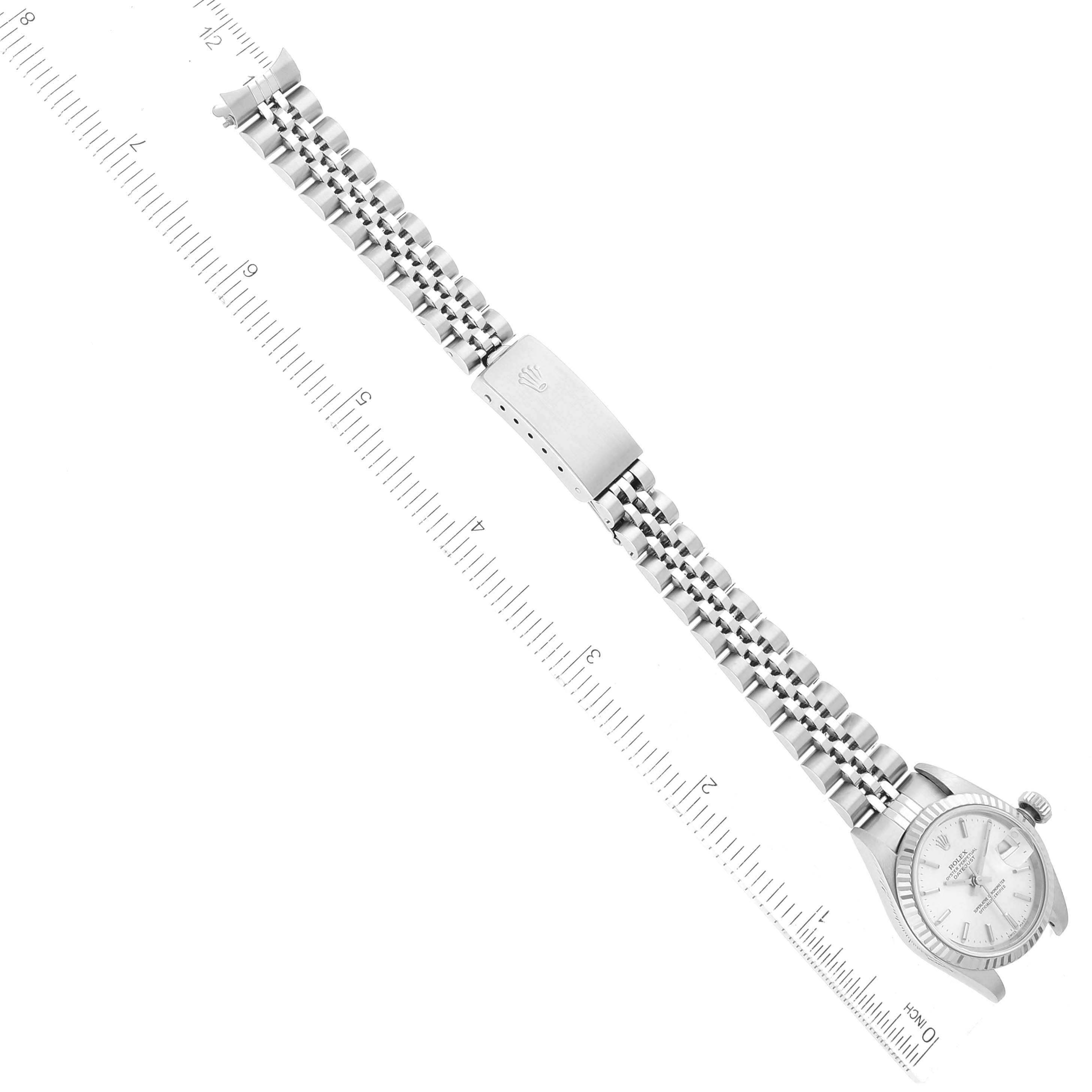 The image shows a top-down view of a Rolex Datejust 79174 Women's Stainless Steel Silver Dial 79174 Women's Stainless Steel Silver Dial watch, highlighting the dial, bezel, bracelet, and clasp next to a measurement scale.
