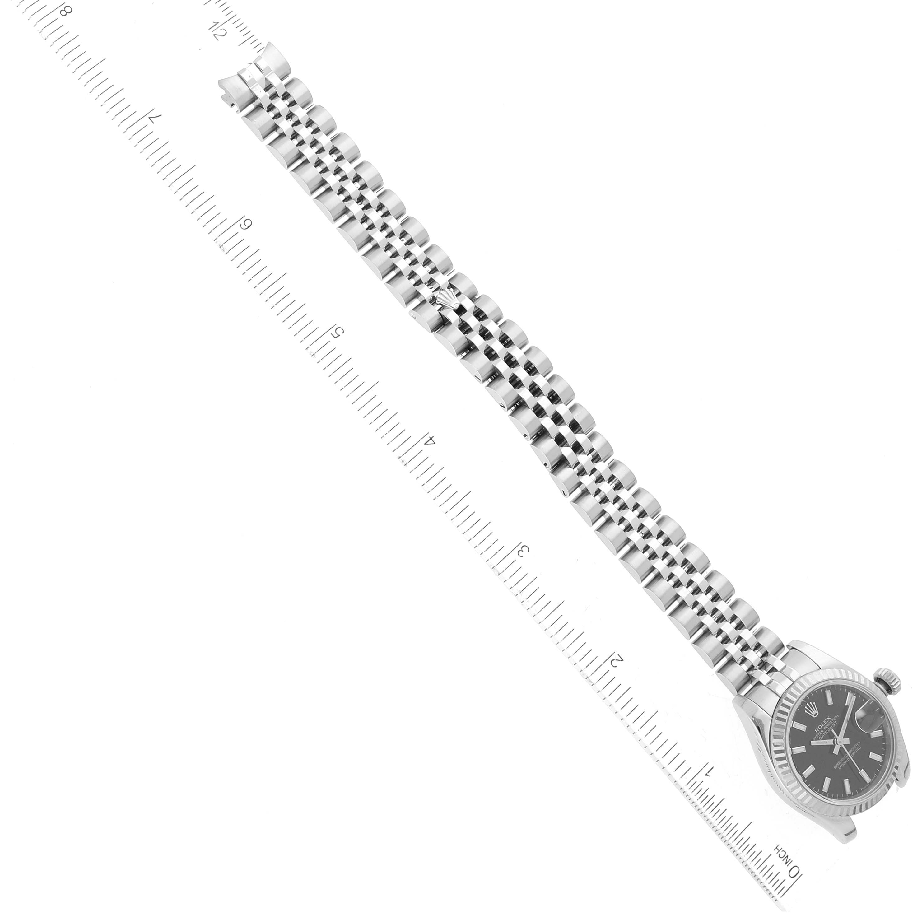 The image shows a Rolex Datejust 179174 Women's Stainless Steel Black Dial 179174 Women's Stainless Steel Black Dial watch, angled to display both the face and the full bracelet alongside a measuring ruler.