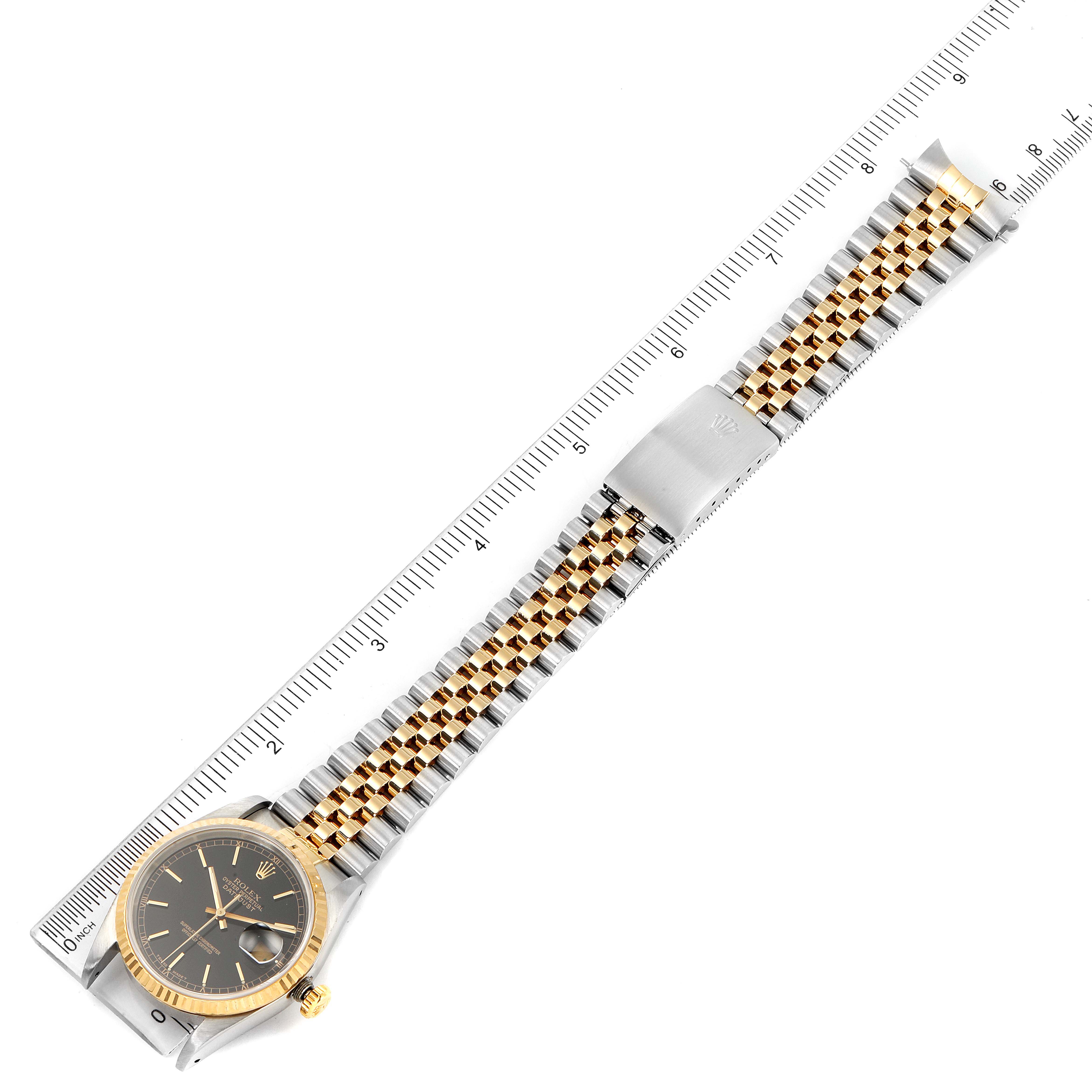 The image shows a Rolex Datejust 16233 Men's Steel and Gold (two tone) Black Dial 16233 Men's Steel and Gold (two tone) Black Dial model watch lying flat with a ruler, displaying the face, bezel, and bracelet at a top-down angle.