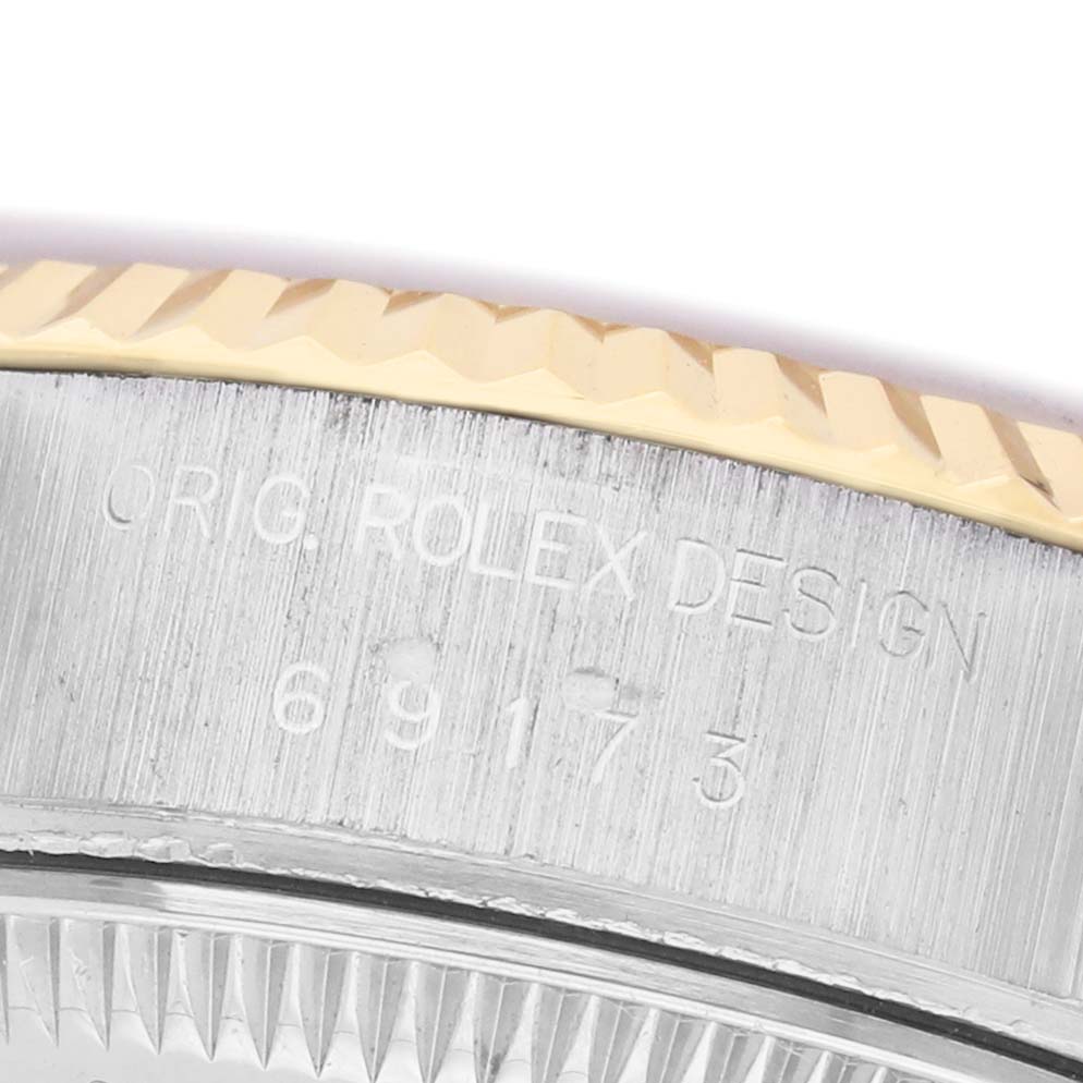 The image shows a close-up of the Rolex Datejust 69173 Women's Steel and Gold (two tone) White Dial model's case side with the engraved text and fluted bezel.