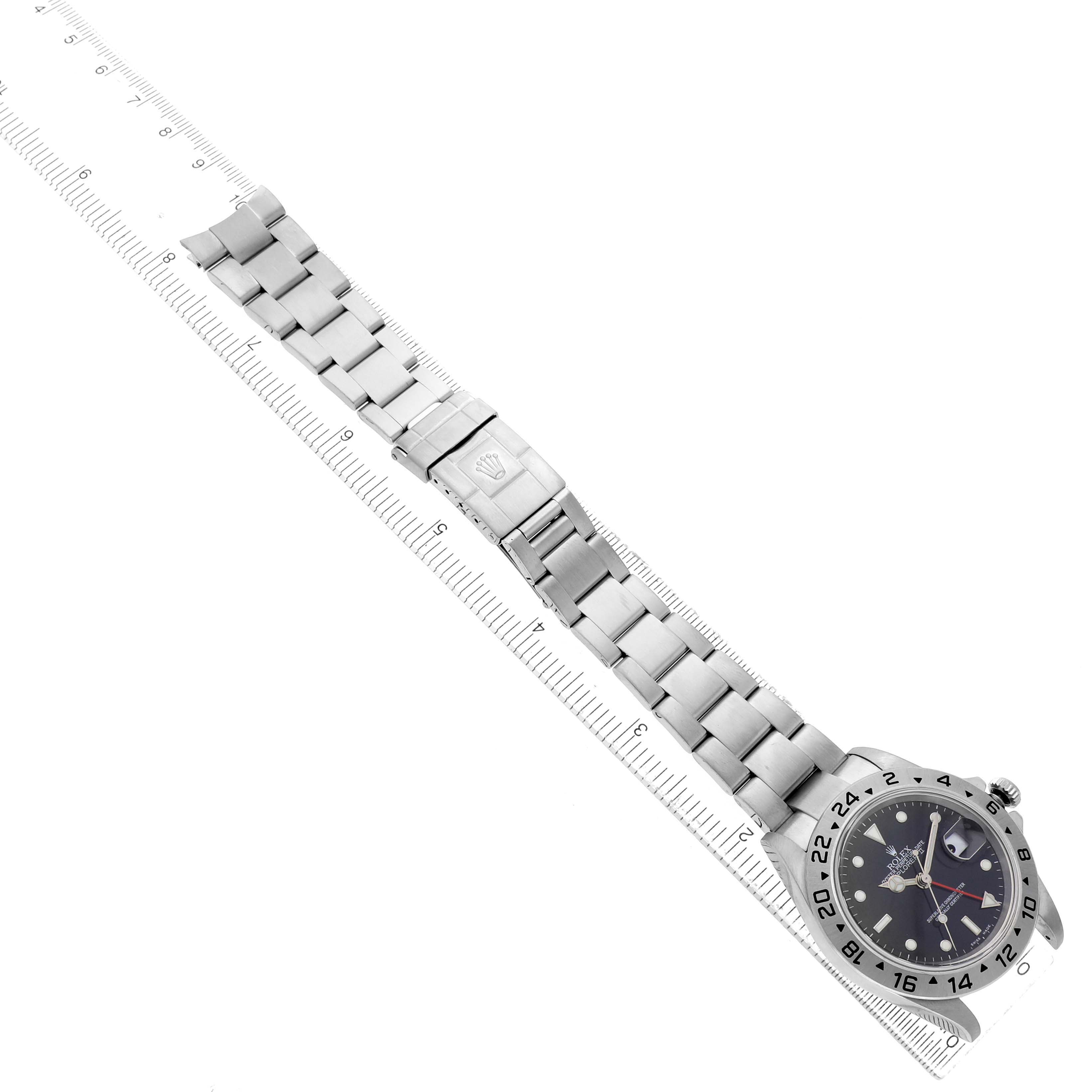 The Rolex Explorer 16570 Men's Stainless Steel Black Dial watch is shown from an angled top view, displaying its face and full metal bracelet laid alongside a ruler.