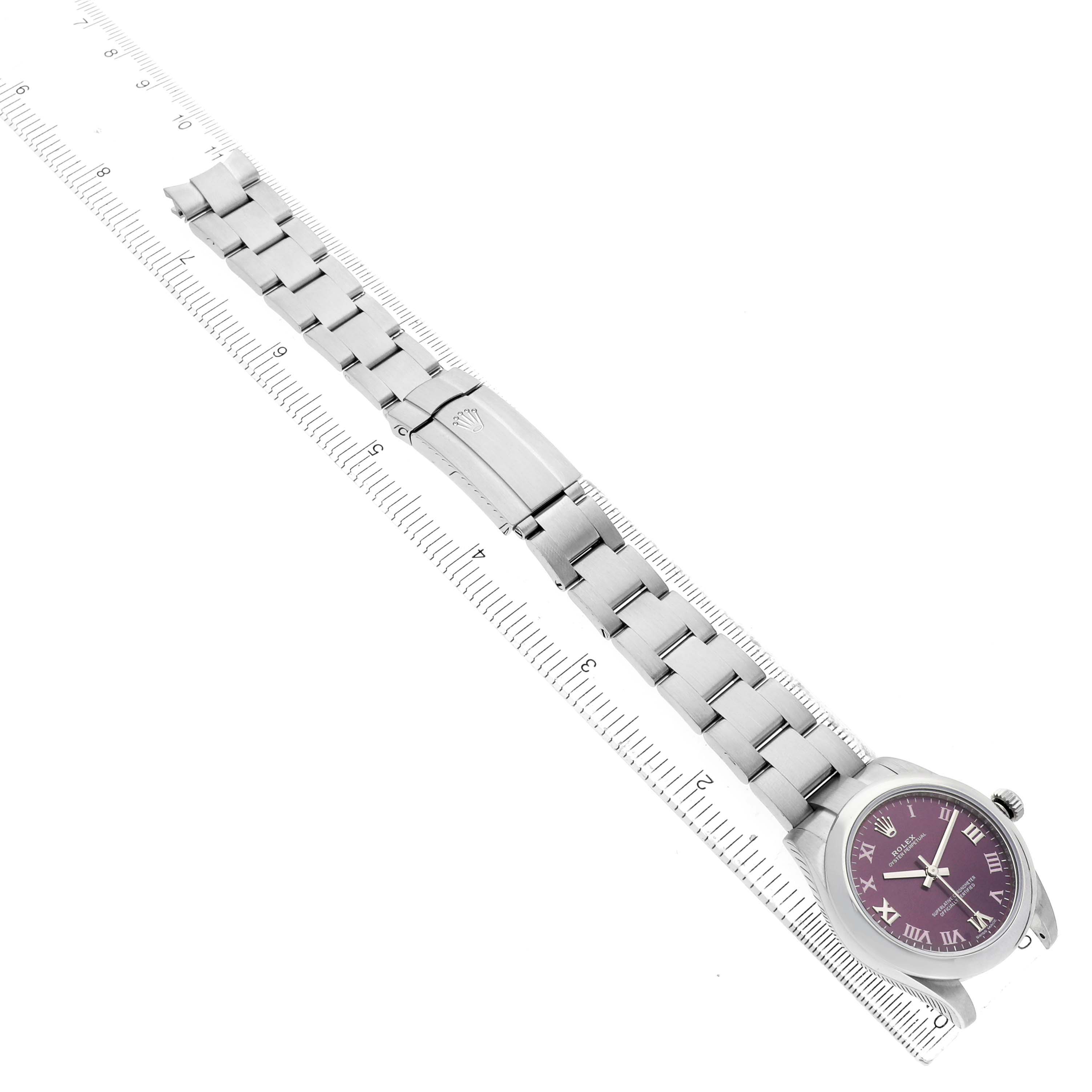 The Rolex Oyster Perpetual 177200 Women's Stainless Steel Purple Dial watch is shown from a top-down angle, including the face, bezel, bracelet, and clasp alongside a ruler.