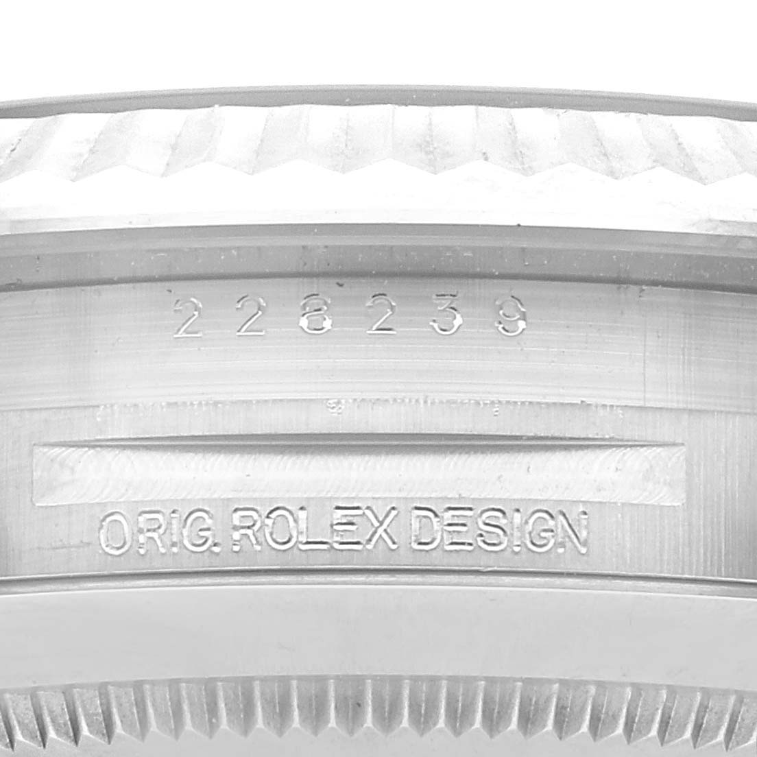 This close-up image of a Rolex President 228239 Men's White Gold Blue Dial 228239 Men's White Gold Blue Dial shows the serial number and part of the bezel with the text "ORIG. ROLEX DESIGN" engraved.