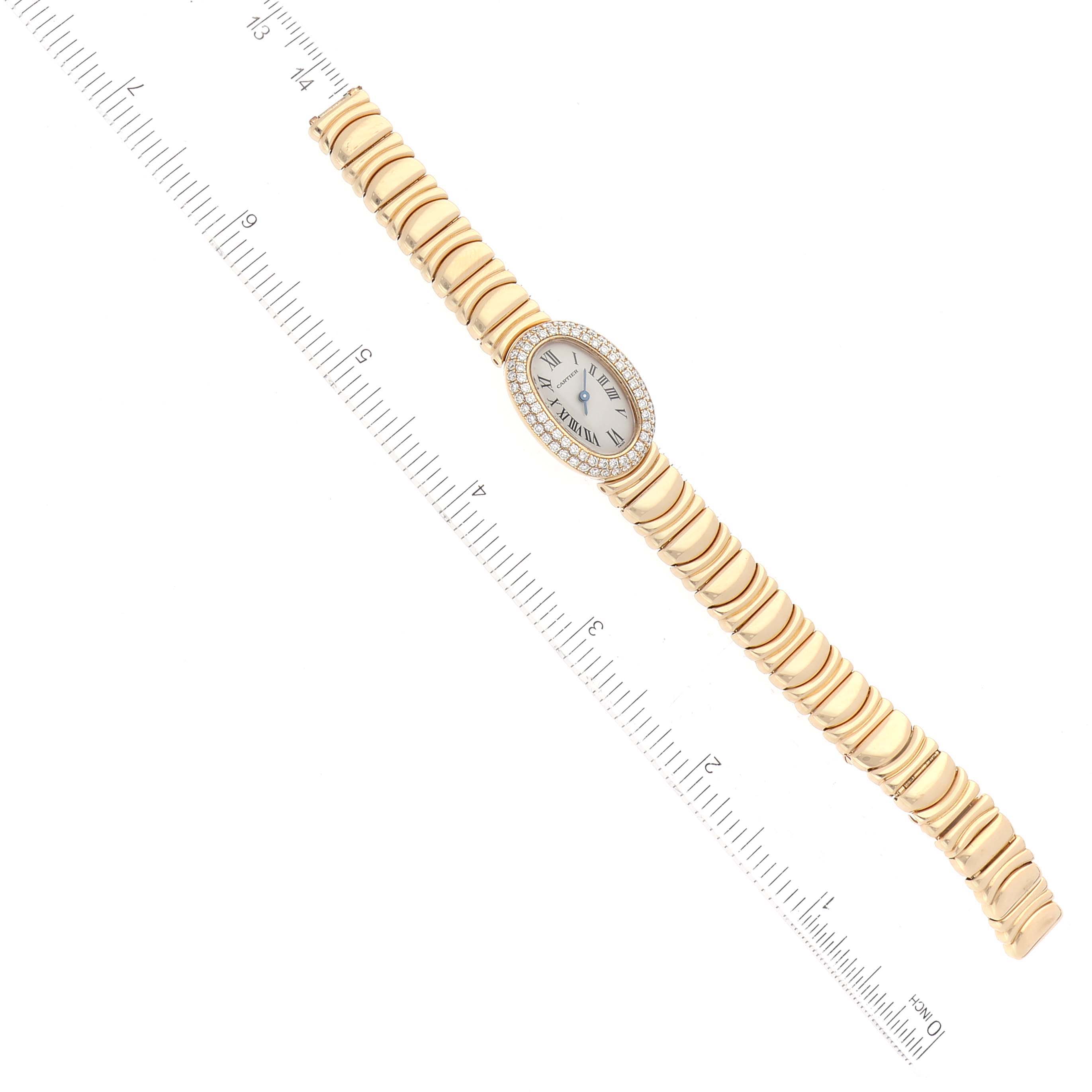 The image shows a top-down view of a Cartier Baignoire WB5094D8 Women's Yellow Gold Silver Dial WB5094D8 Women's Yellow Gold Silver Dial watch with its face and gold bracelet, alongside a measuring ruler.