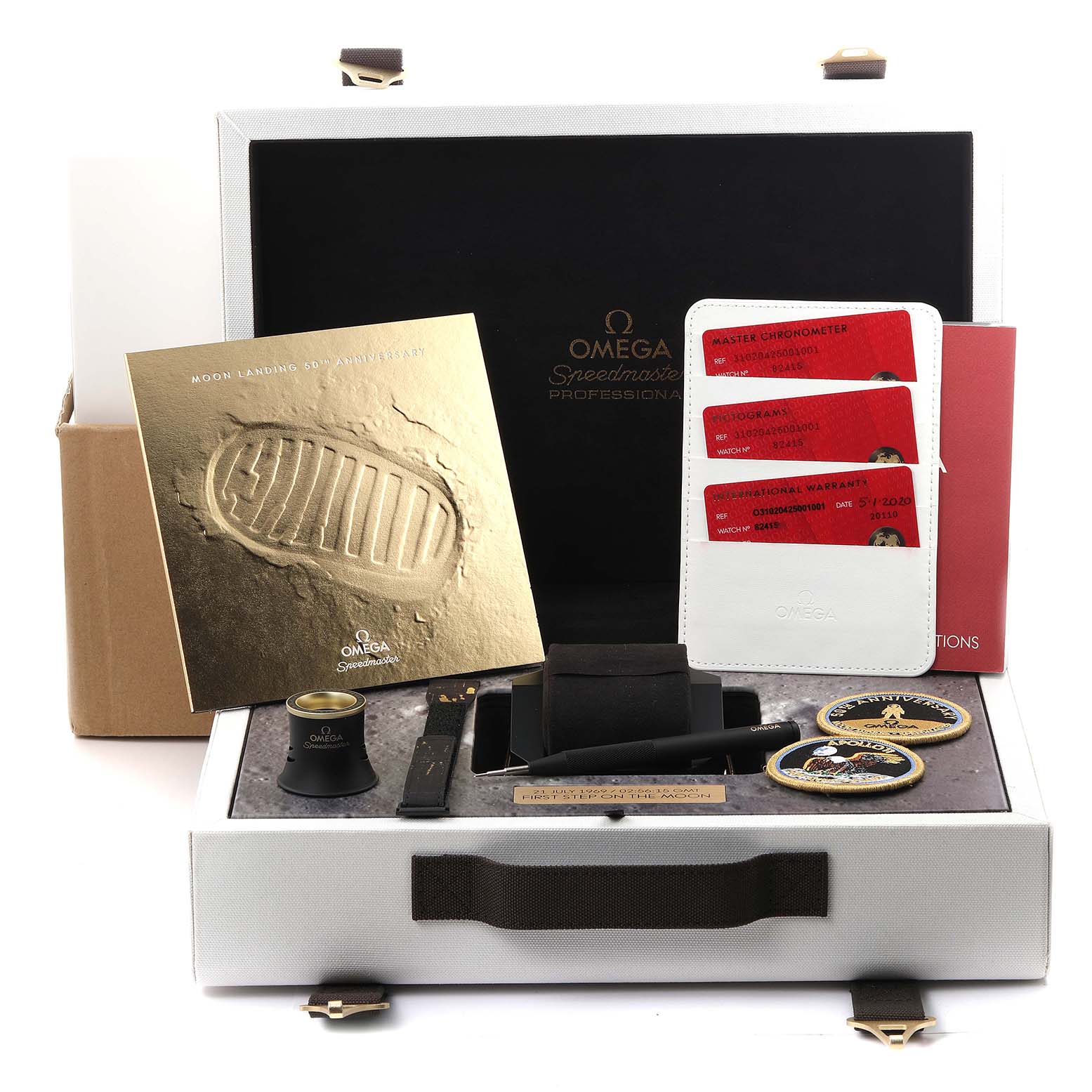 The Omega Speedmaster 310.20.42.50.01.001 Men's Stainless Steel Grey Dial 310.20.42.50.01.001 Men's Stainless Steel Grey Dial package includes the box, papers, a magnifying loupe, NATO strap, and mission patches, viewed from the top.