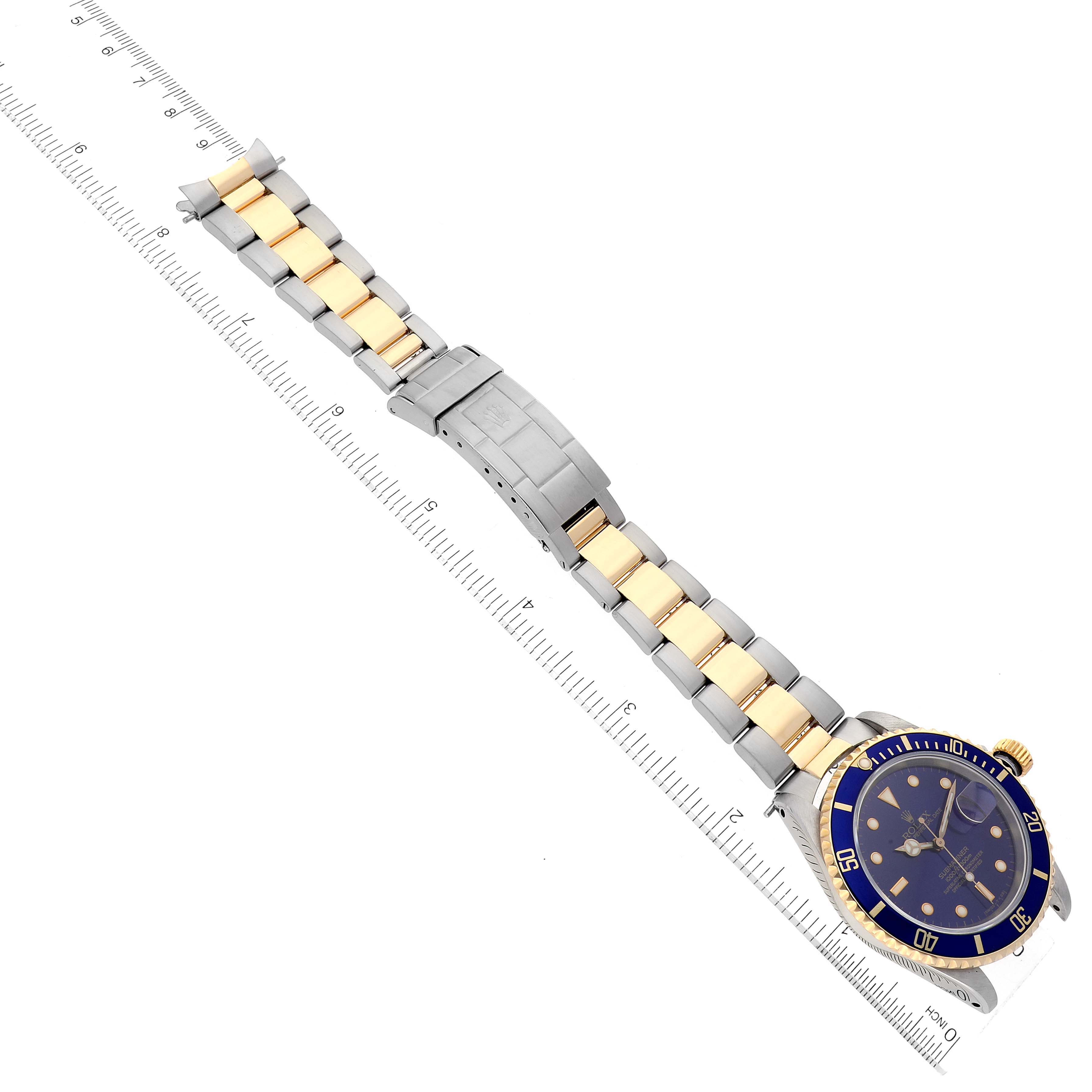 This image shows a Rolex Submariner 16613 Men's Steel and Gold (two tone) Blue Dial 16613 Men's Steel and Gold (two tone) Blue Dial watch laid flat, with the full bracelet and clasp visible, alongside a measuring ruler.