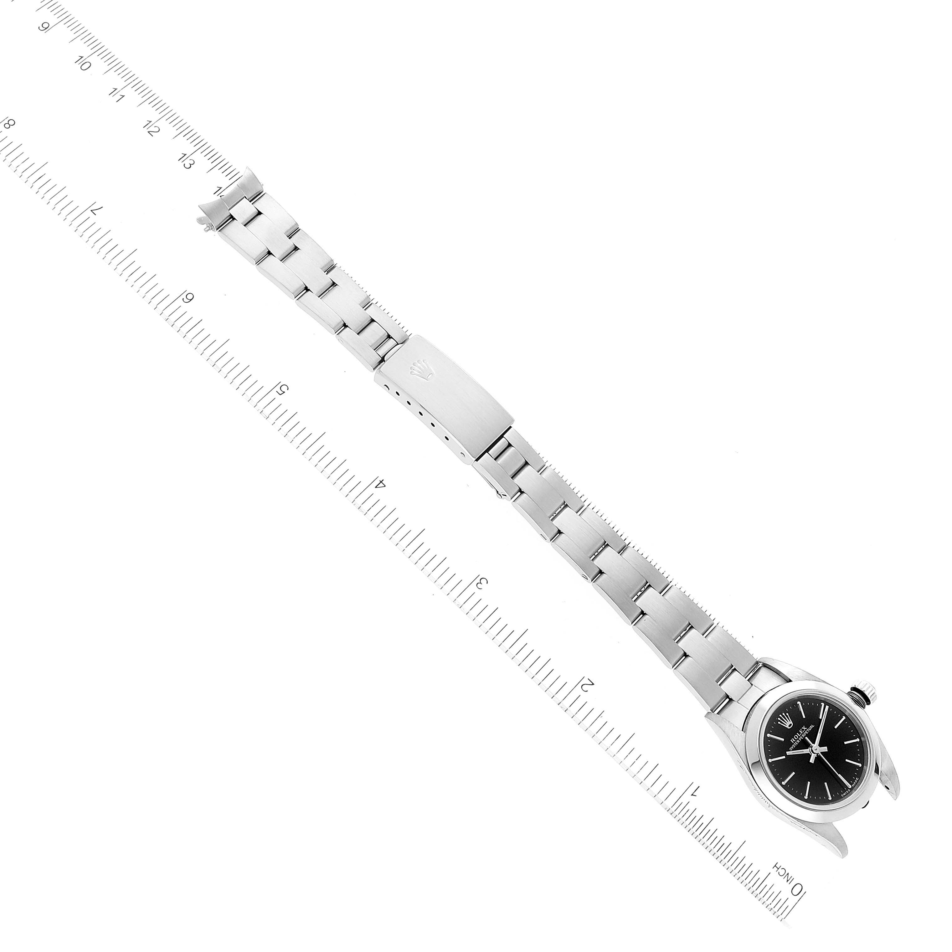 This image shows the Rolex Oyster Perpetual 76080 Women's Stainless Steel Black Dial 76080 Women's Stainless Steel Black Dial watch laid flat, featuring its bracelet, clasp, and dial, with a ruler for scale.