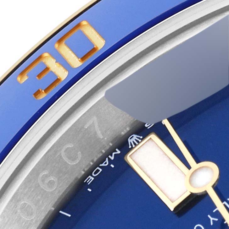 The close-up angle of the Rolex Submariner 126613LB Men
s Steel and Gold (two tone) Blue Dial 126613LB Men
s Steel and Gold (two tone) Blue Dial watch shows the bezel, part of the dial, and the minute hand.