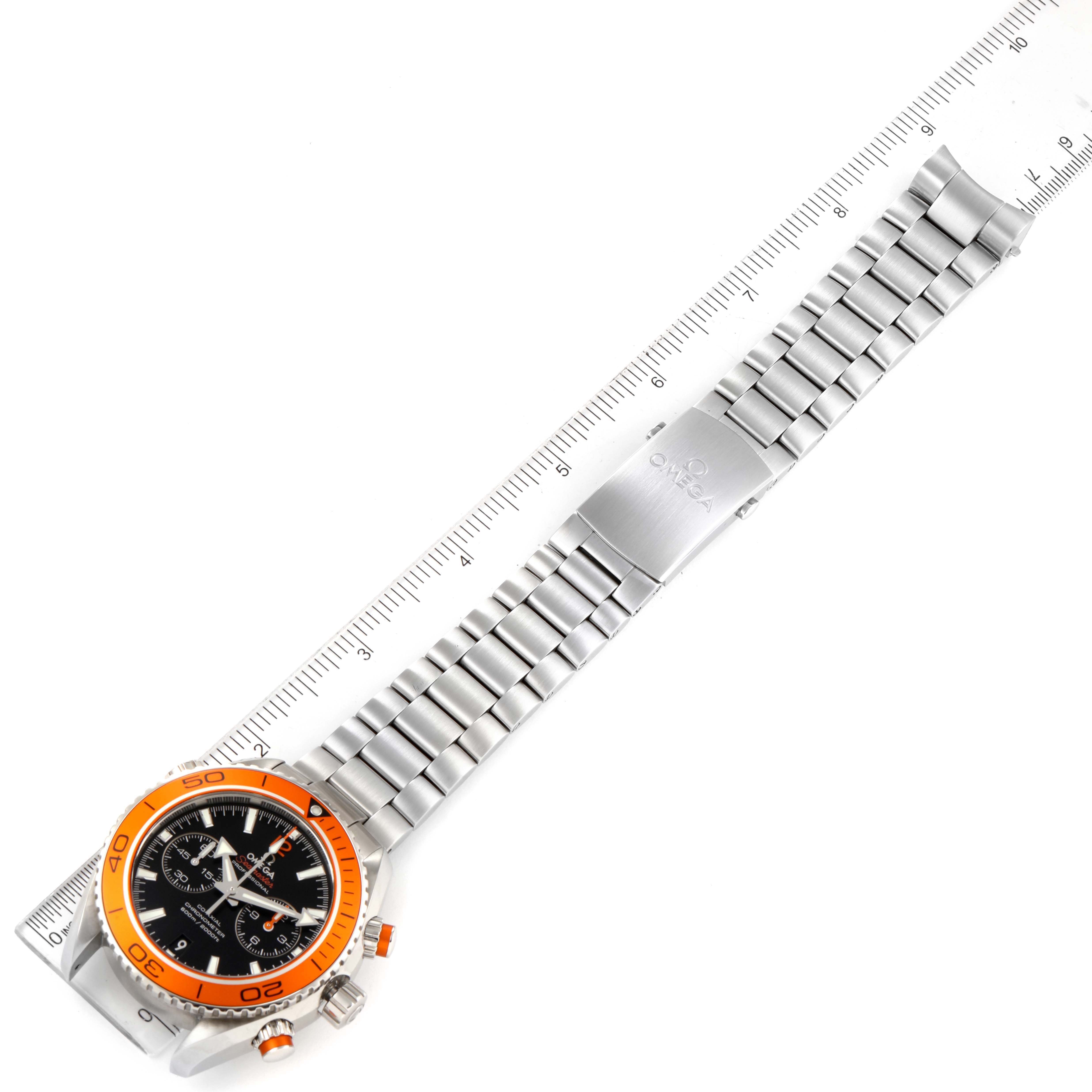 The image shows the Omega Planet Ocean 232.30.46.51.01.002 Men's Stainless Steel Black Dial 232.30.46.51.01.002 Men's Stainless Steel Black Dial watch with an orange bezel and a full stainless steel bracelet, laid flat against a ruler.