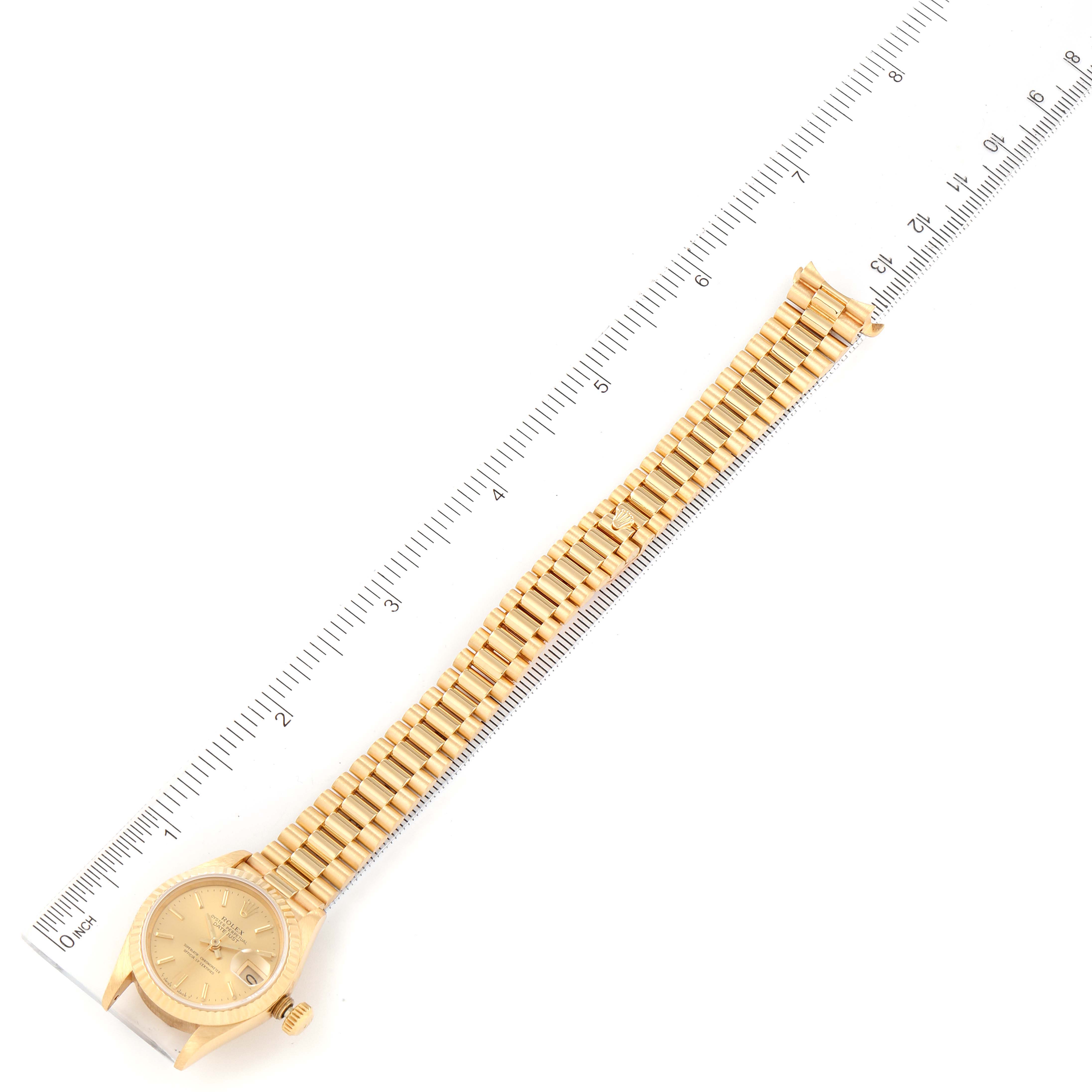 The image shows a Rolex President 69178 Women
s Yellow Gold Champagne Dial 69178 Women
s Yellow Gold Champagne Dial model watch lying flat next to a ruler, displaying the watch dial and bracelet.
