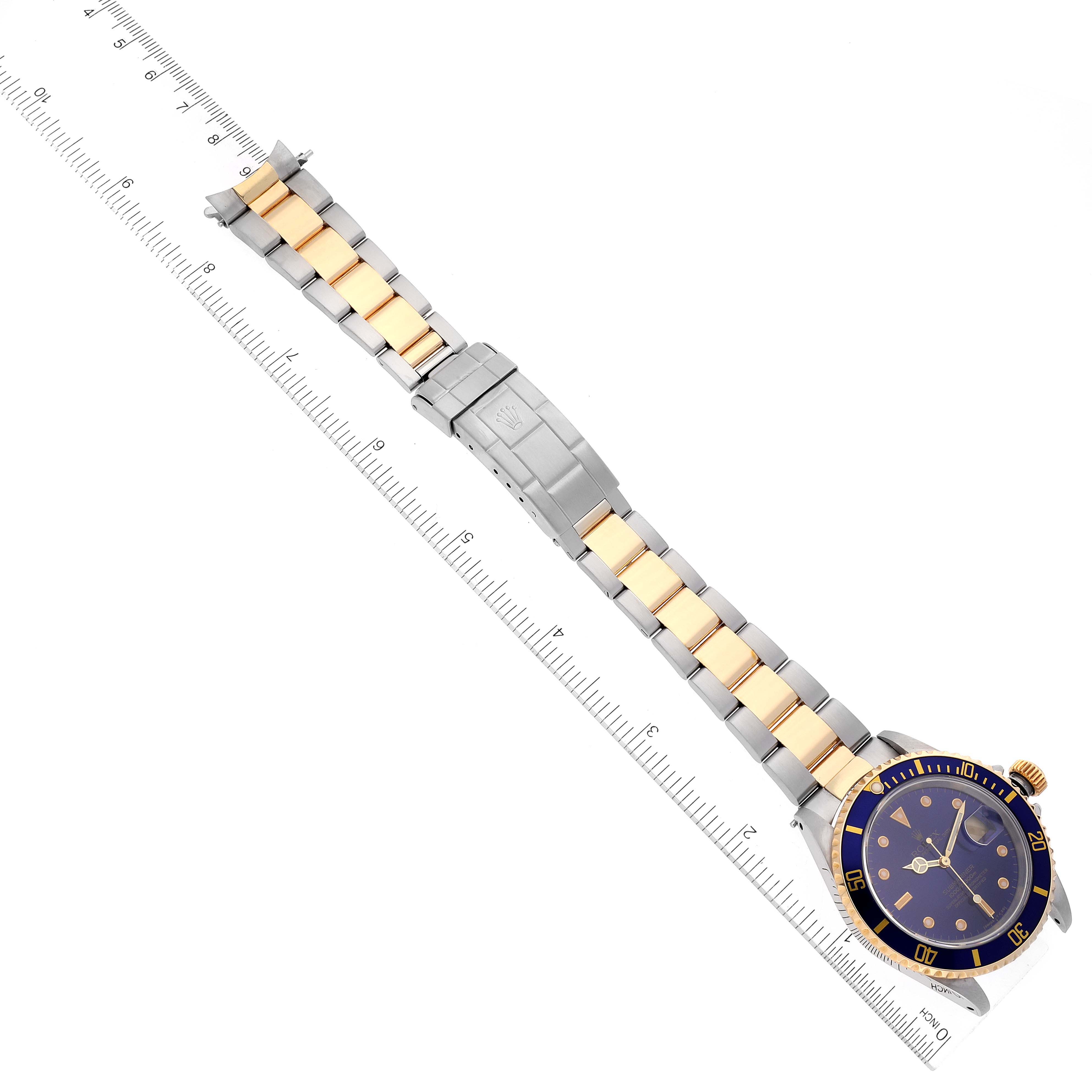 The image shows a top view of a Rolex Submariner 16613 Men's Steel and Gold (two tone) Blue Dial 16613 Men's Steel and Gold (two tone) Blue Dial watch, highlighting the bracelet, clasp, and face, alongside a ruler for size reference.