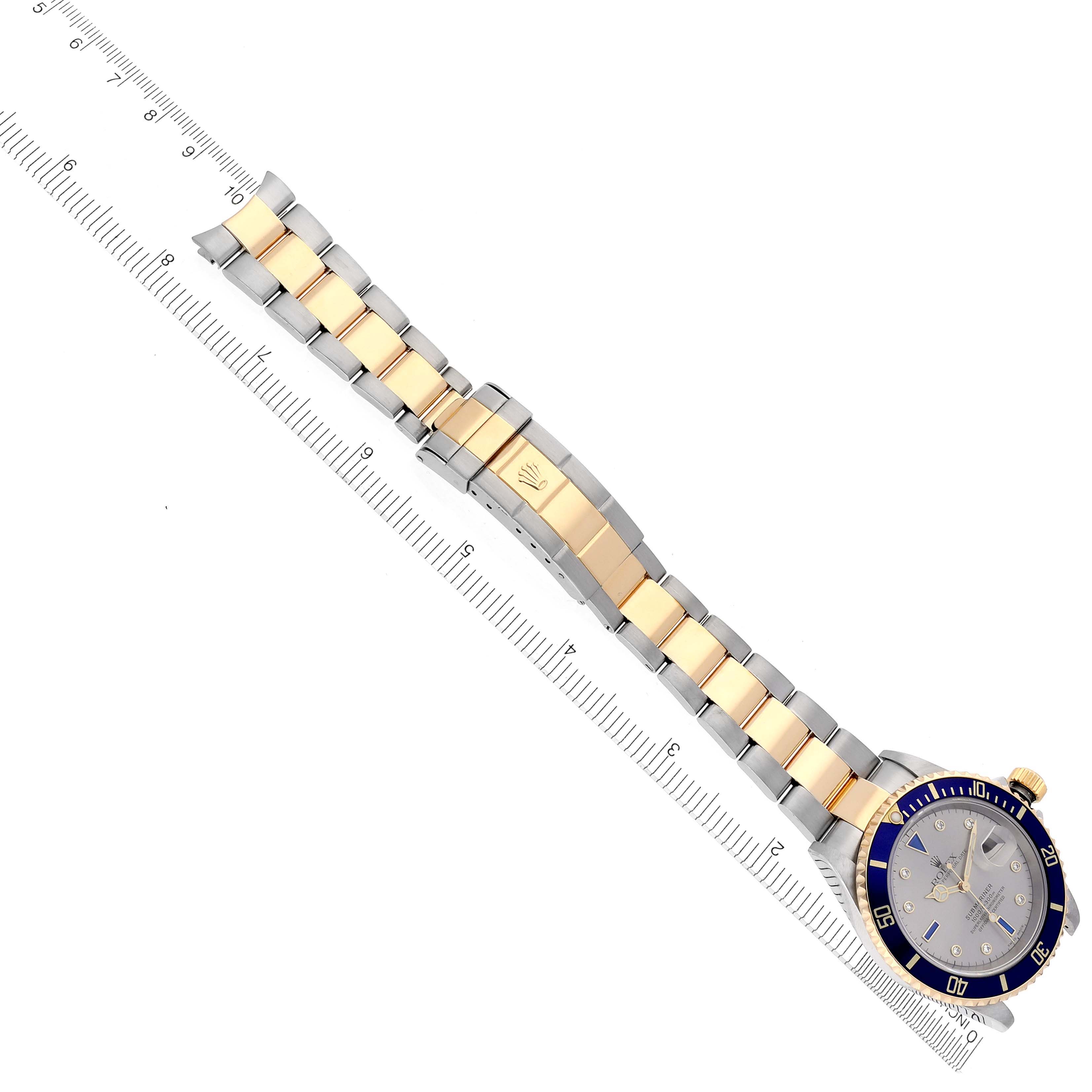 The Rolex Submariner 16613 Men's Steel and Gold (two tone) Silver Dial 16613 Men's Steel and Gold (two tone) Silver Dial watch is displayed from an angled top view, showing the face, case, and full two-tone bracelet alongside a ruler.