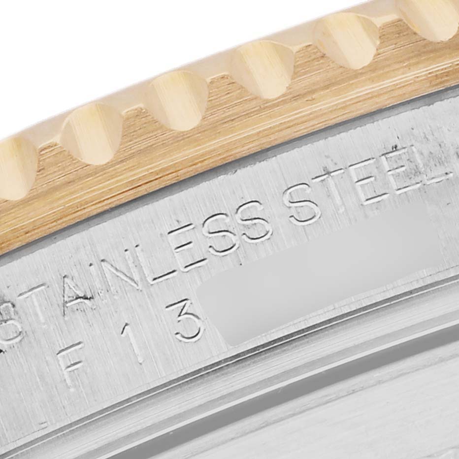 The image shows a close-up angle of the Rolex Submariner 16613 Men's Steel and Gold (two tone) Silver Dial 16613 Men's Steel and Gold (two tone) Silver Dial's gold bezel edge and stainless steel case back engraved with text.