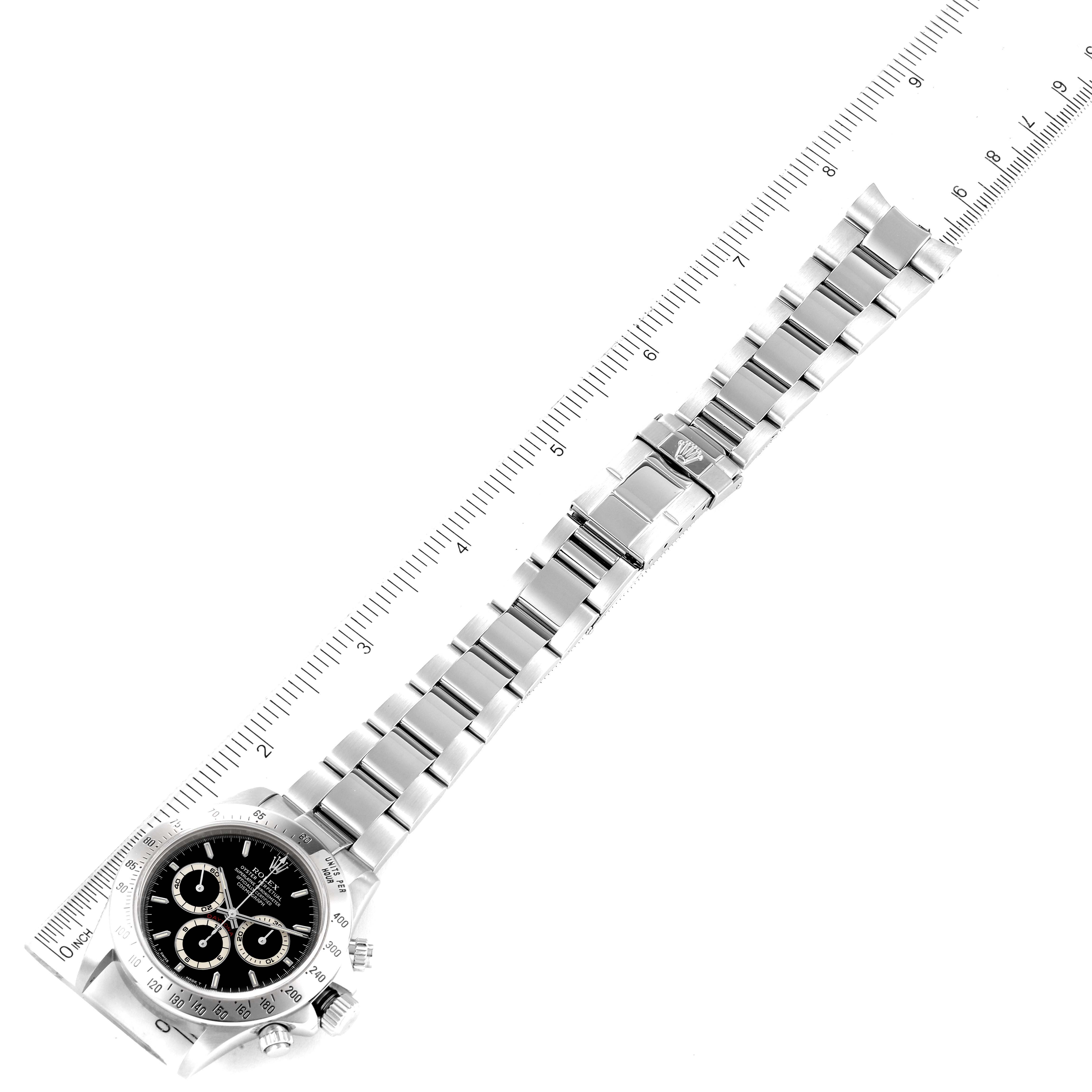 The image shows a Rolex Daytona 16520 Men's Stainless Steel Black Dial watch from an overhead angle, displaying the face, bezel, and full metal bracelet next to a ruler.