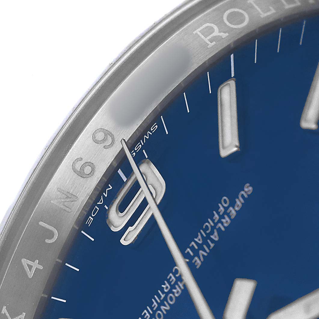 The image shows a close-up of the Rolex Oyster Perpetual 116000 Men's Stainless Steel Blue Dial watch, highlighting a portion of the blue dial and bezel.