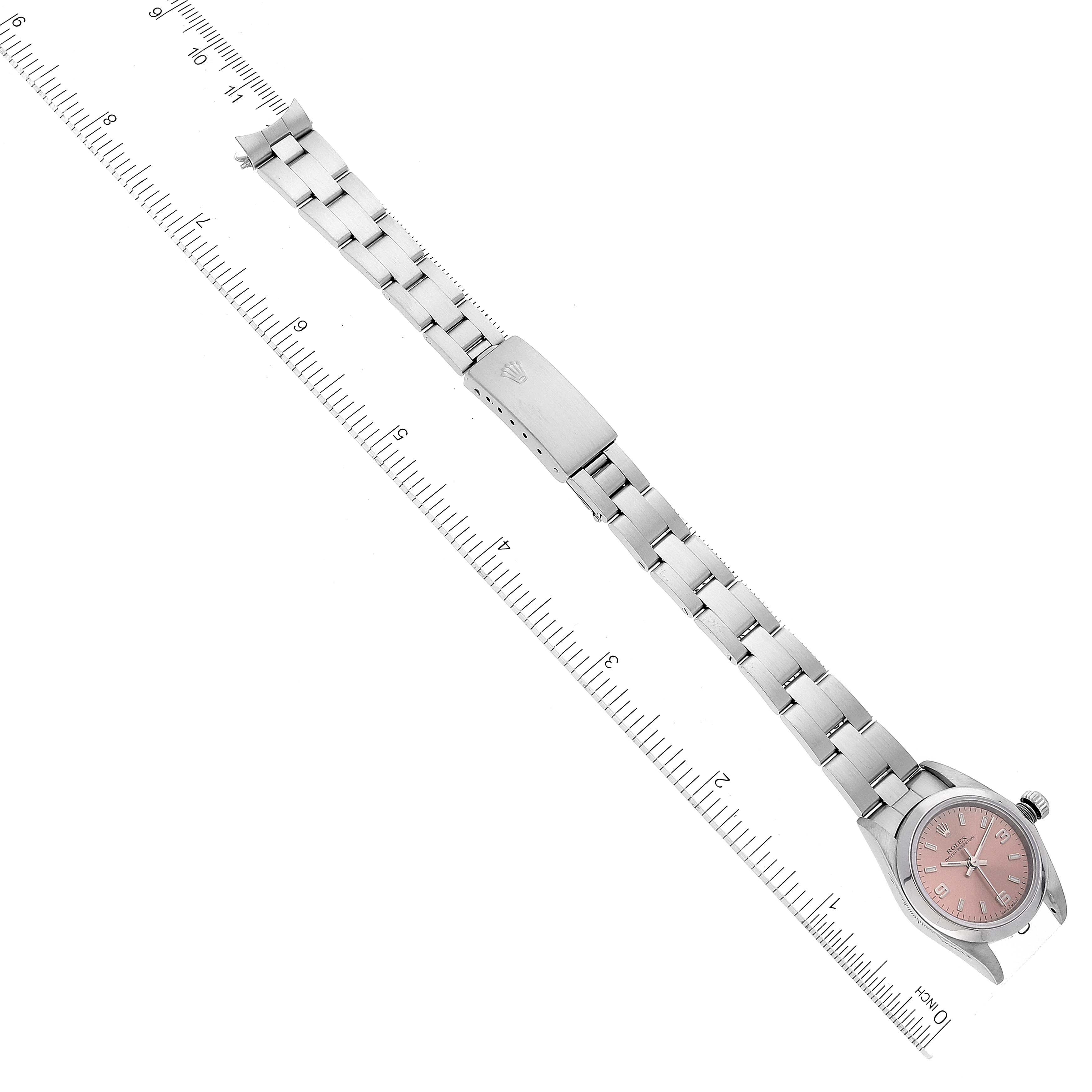 The image shows a Rolex Oyster Perpetual 76080 Women
s Stainless Steel Pink Dial 76080 Women
s Stainless Steel Pink Dial watch laid flat with its pink dial, metal bracelet, and clasp visible alongside a ruler.