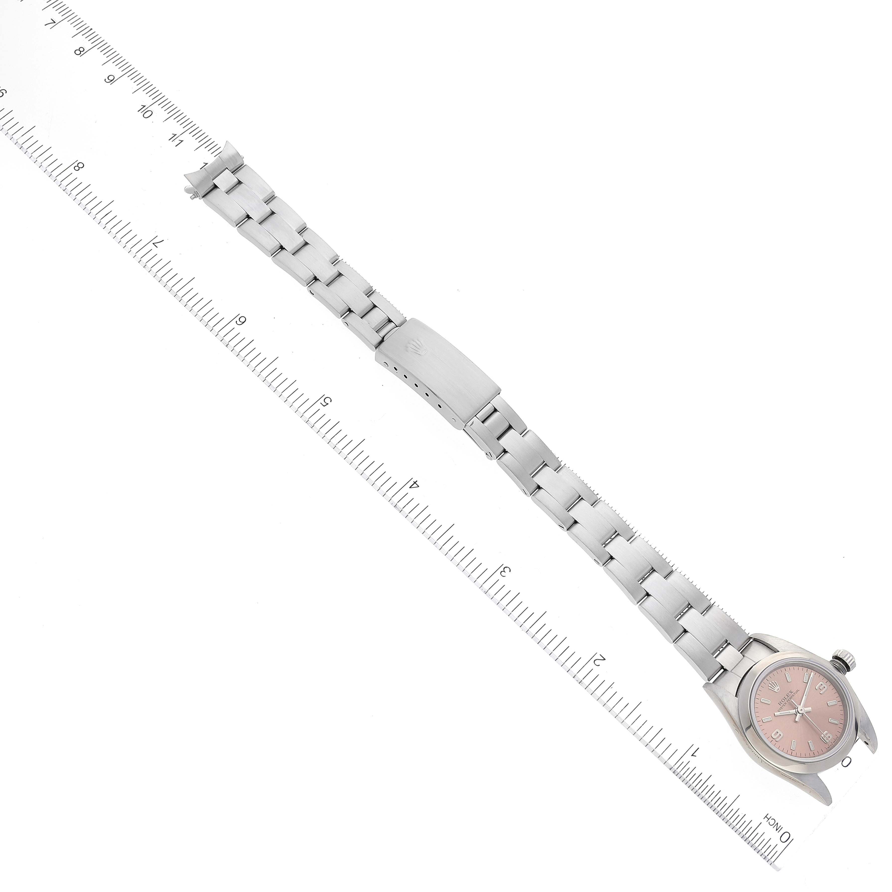 The image shows a Rolex Oyster Perpetual 76080 Women
s Stainless Steel Pink Dial 76080 Women
s Stainless Steel Pink Dial watch laid flat with its bracelet extended next to a ruler for scale.
