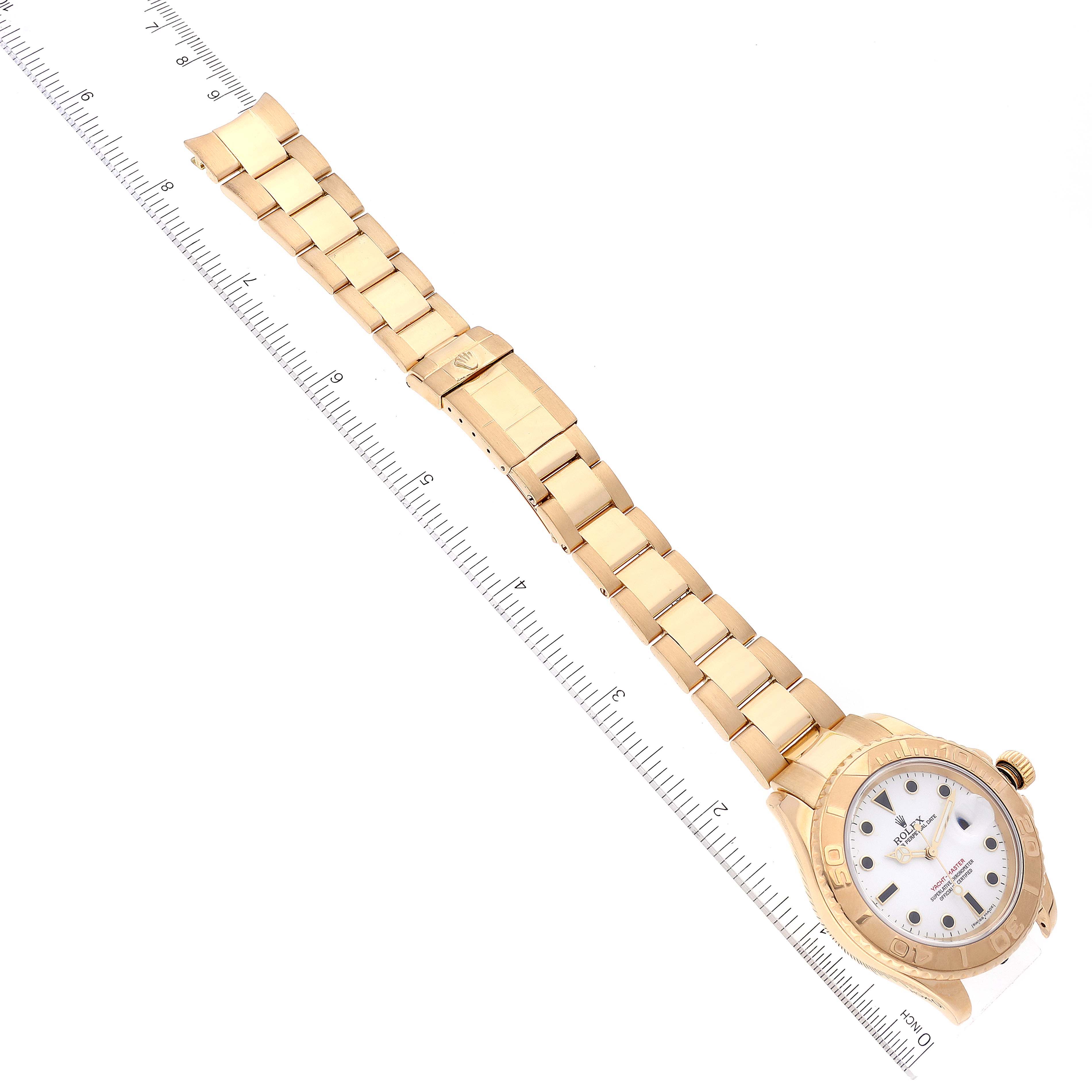 The image shows a Rolex Yacht-Master 16628 Men's Yellow Gold White Dial 16628 Men's Yellow Gold White Dial watch with a gold bracelet displayed diagonally next to a ruler for scale.