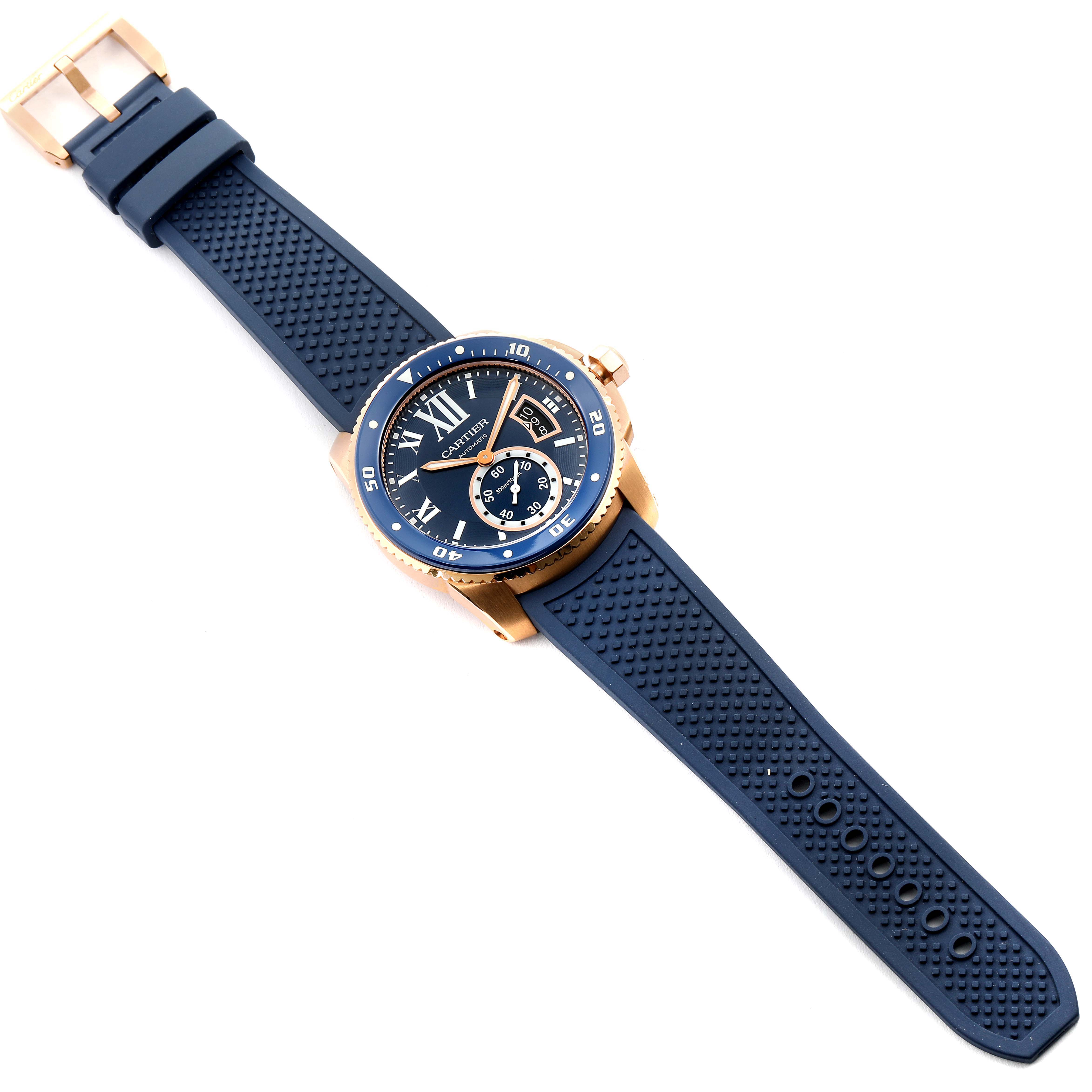 The Calibre de Cartier watch by Cartier is displayed at a slight angle, showing its blue rubber strap and gold-toned bezel.